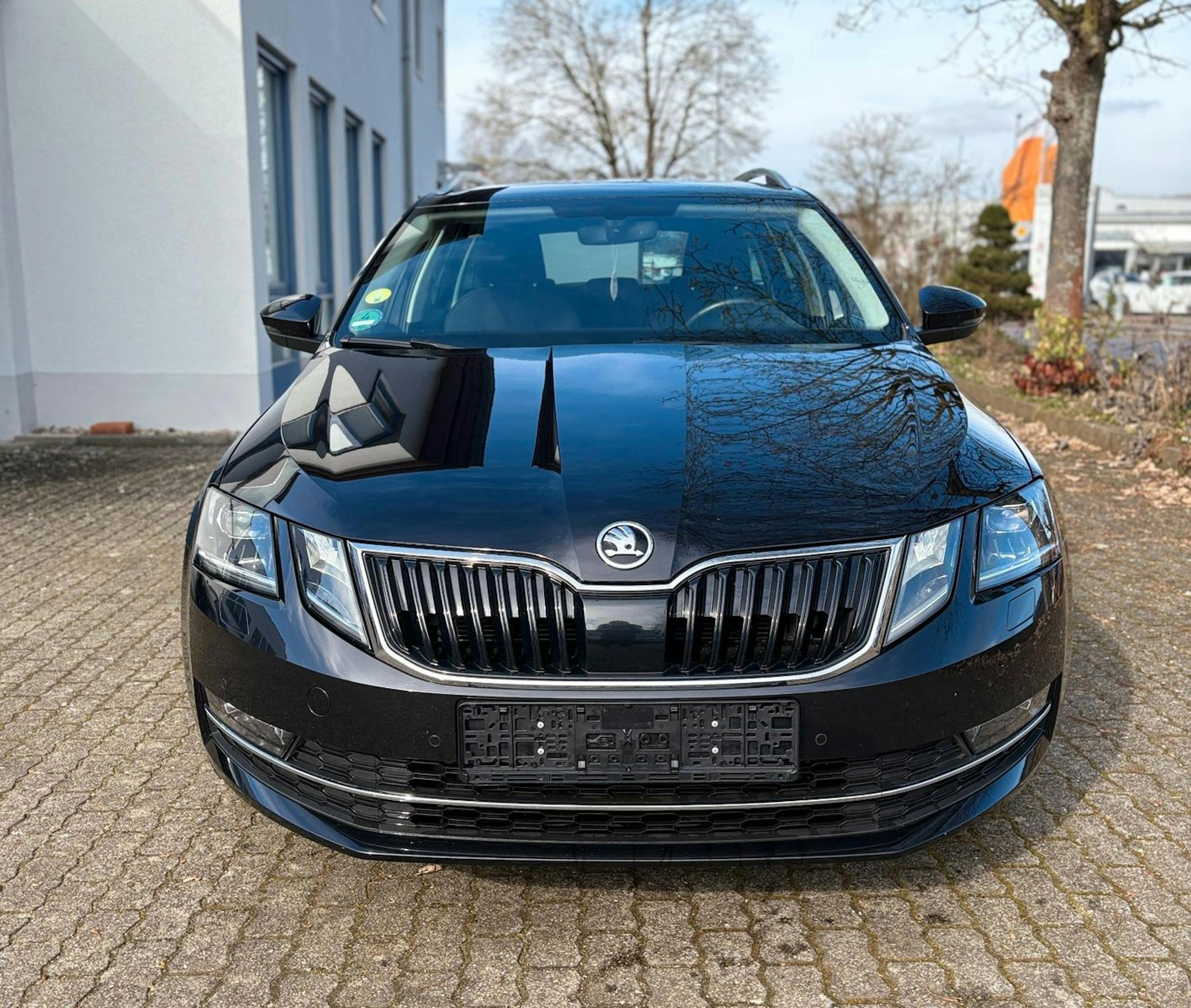 Ein schwarzer Škoda Octavia Kombi steht auf einem gepflasterten Parkplatz vor einem Gebäude