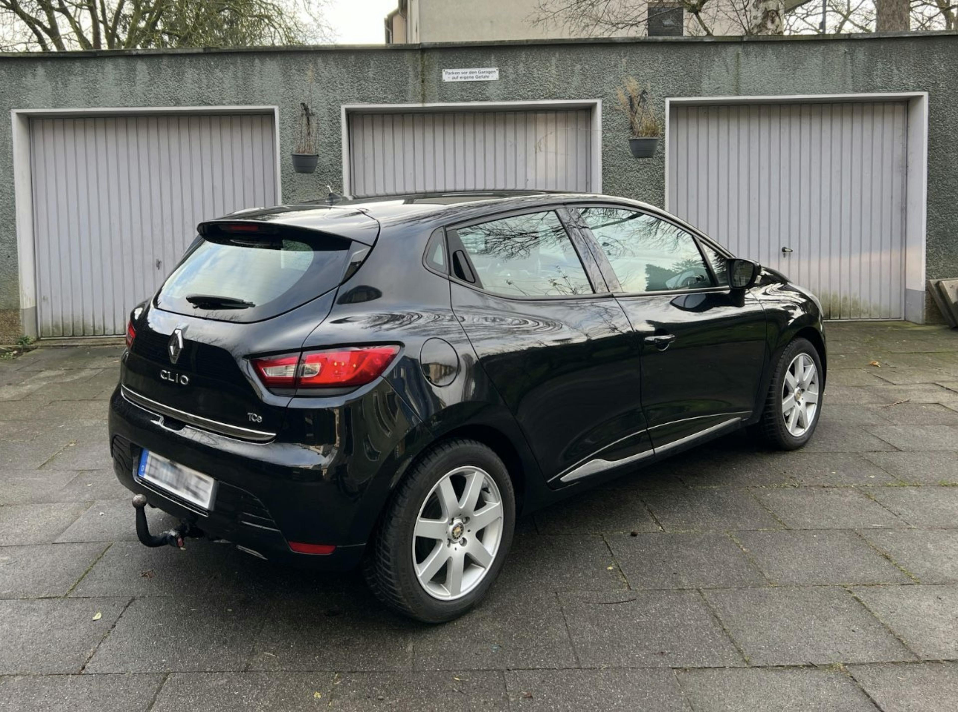 Schwarzer Renault Clio stehend auf einer gepflasterten Fläche vor Garagentoren.