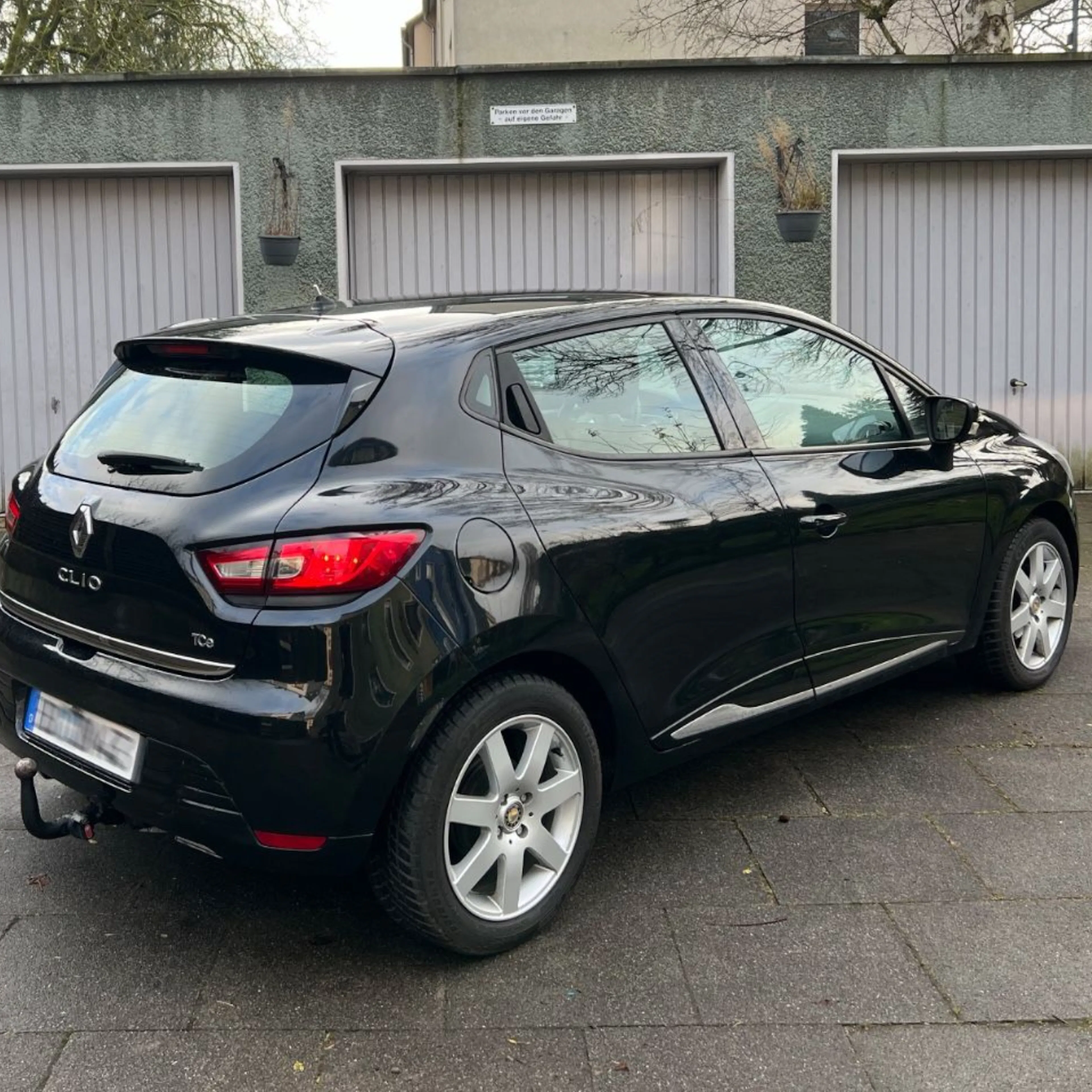 Schwarzer Renault Clio stehend auf einer gepflasterten Fläche vor Garagentoren.