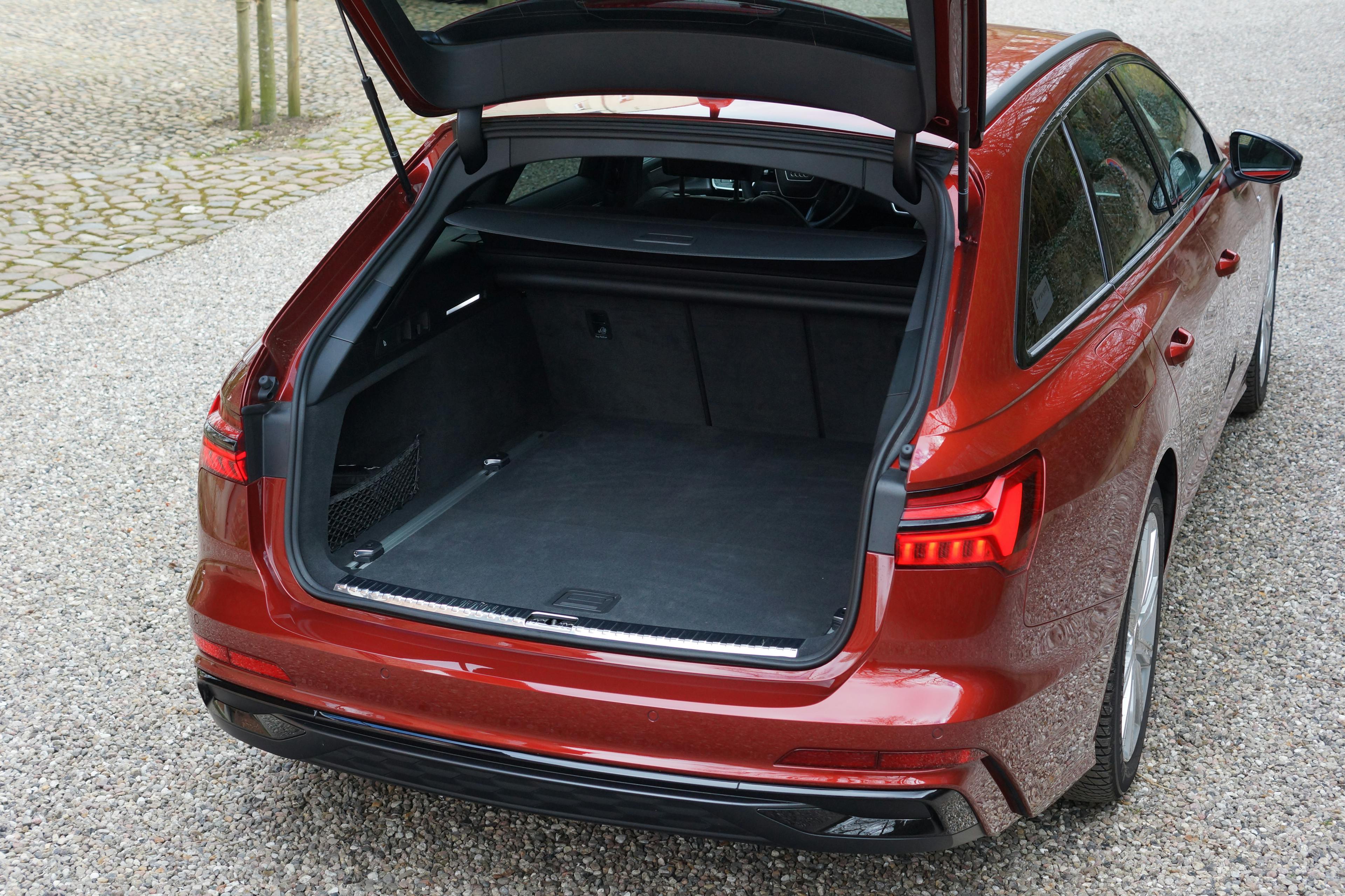 Detailansicht des Kofferraums eines roten Audi A6 Avant C8, der mit geöffneter Heckklappe auf einem Kiesplatz steht.