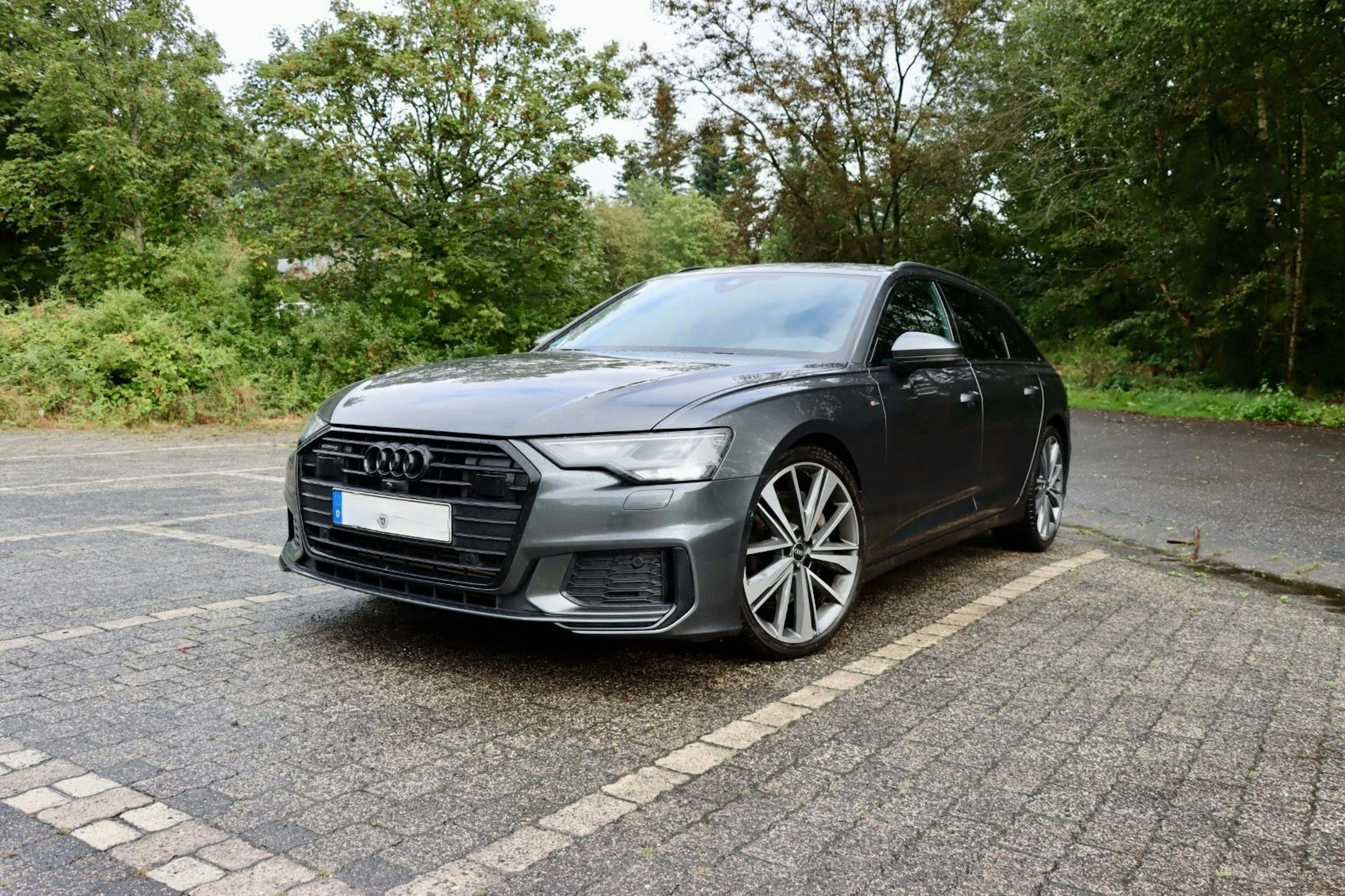 Schwarzer Audi A6 Avant auf einer Asphaltfläche stehend, mit winterlicher Vegetation im Hintergrund.