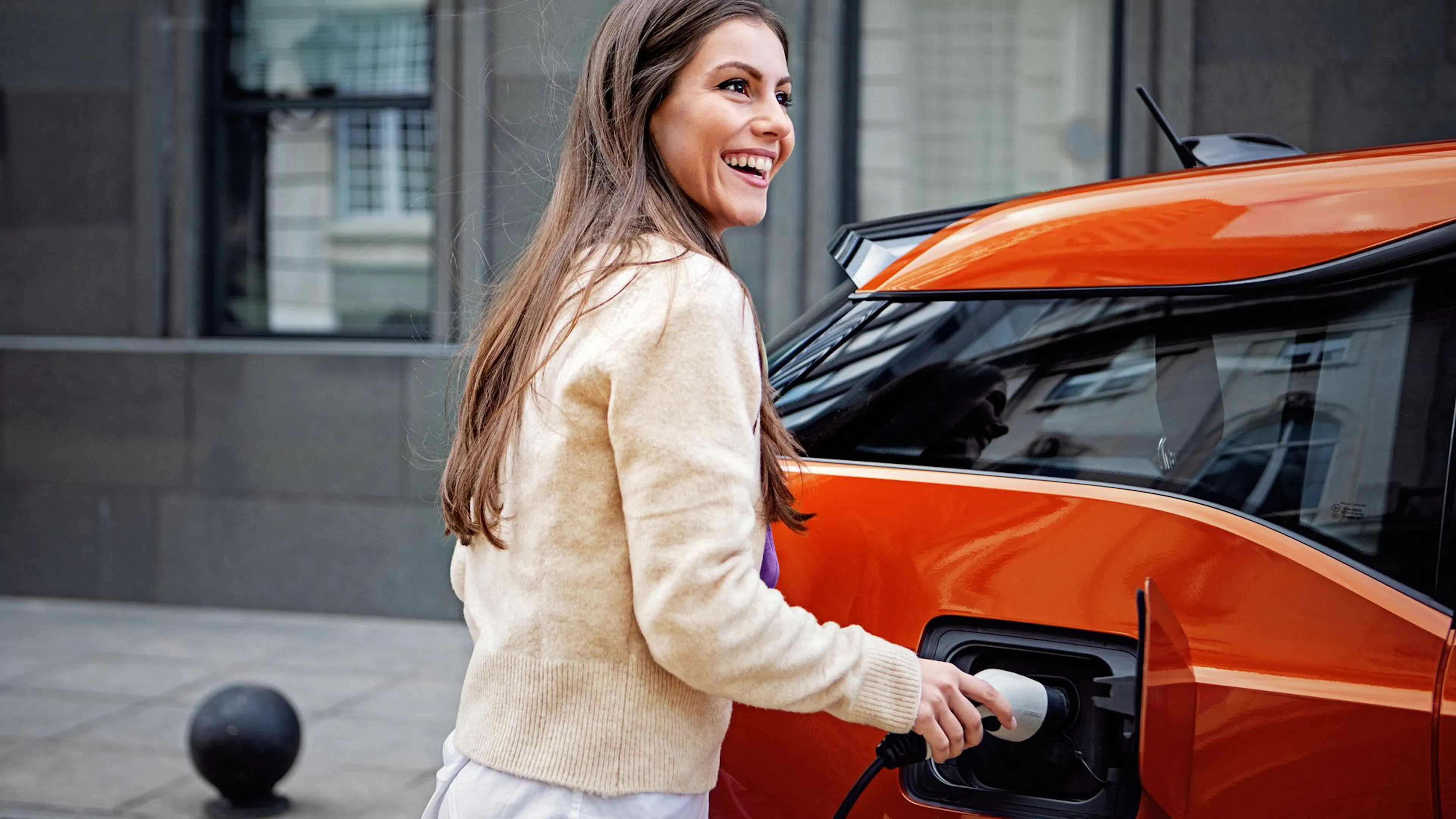 Eine jüngere Frau lädt ein rotes E-Auto.