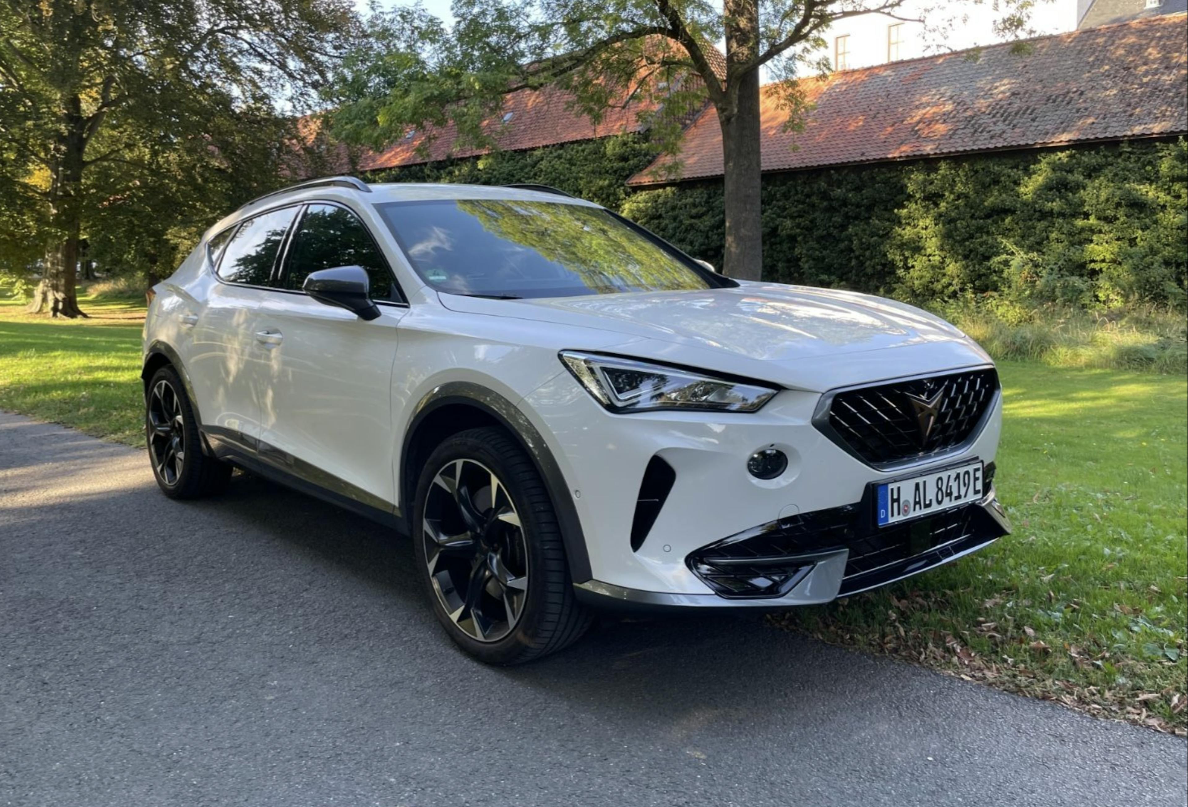 Weißer Cupra Formentor stehend auf einer Asphaltfläche vor Wohnbebauung