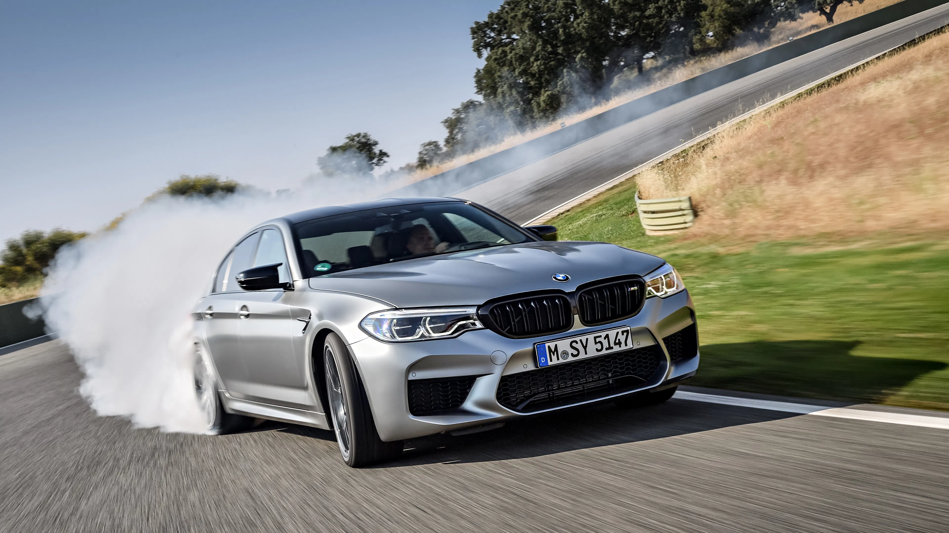 Ein silberner BMW M5 Performance nimmt auf einer Rennstrecke eine Kurve im Drift.