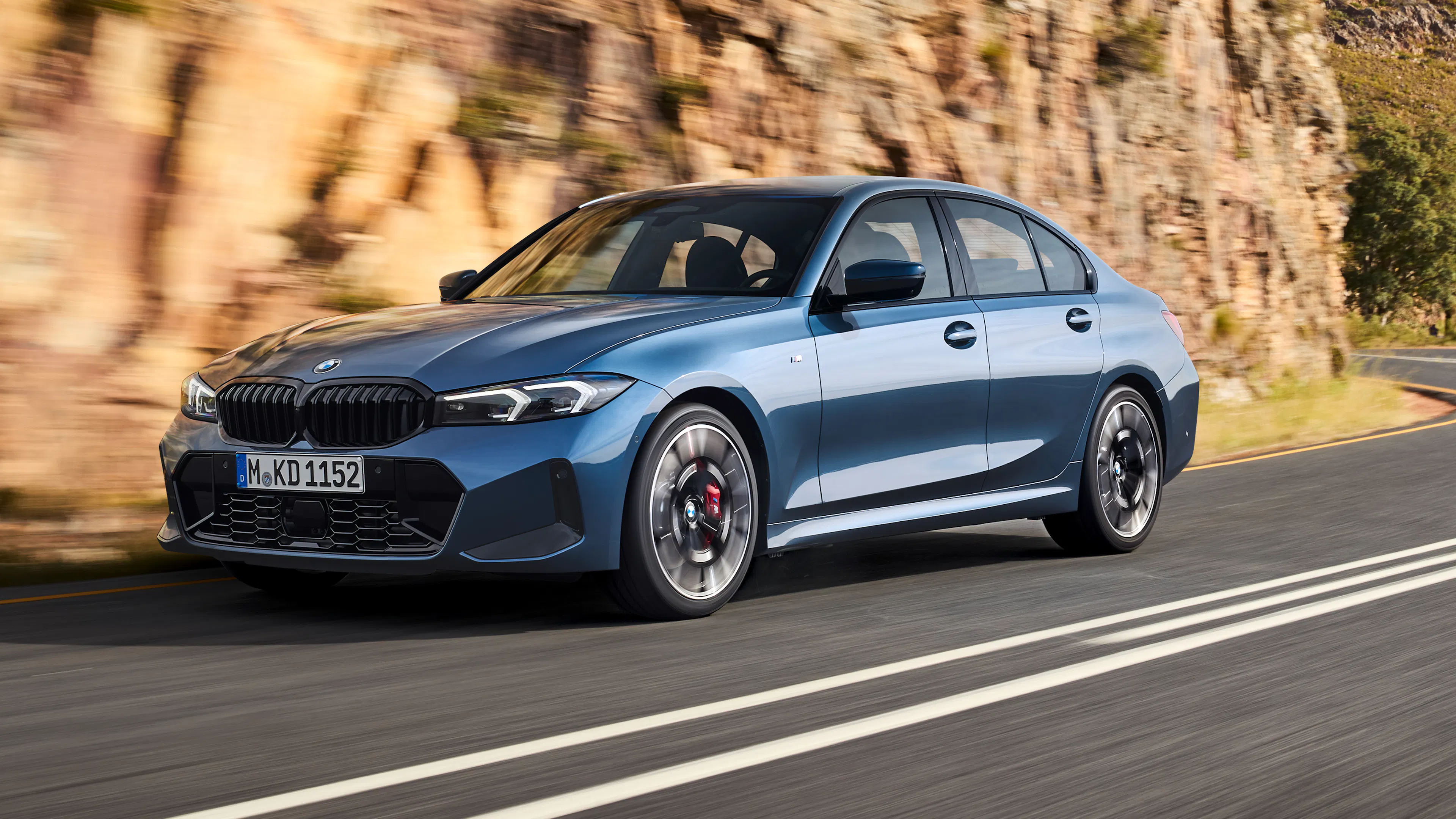 Ein blauer BMW 3er fährt auf einer Landstraße durch ein Gebirge.