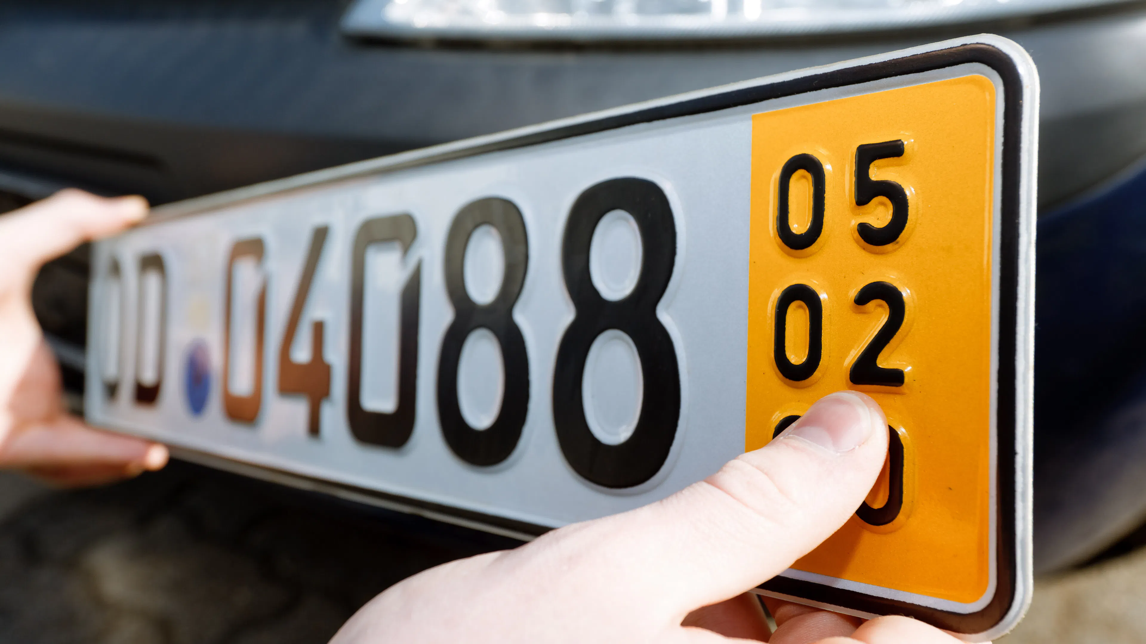 Ein Kurzzeitkennzeichen wird von zwei Händen vor ein Auto gehalten.