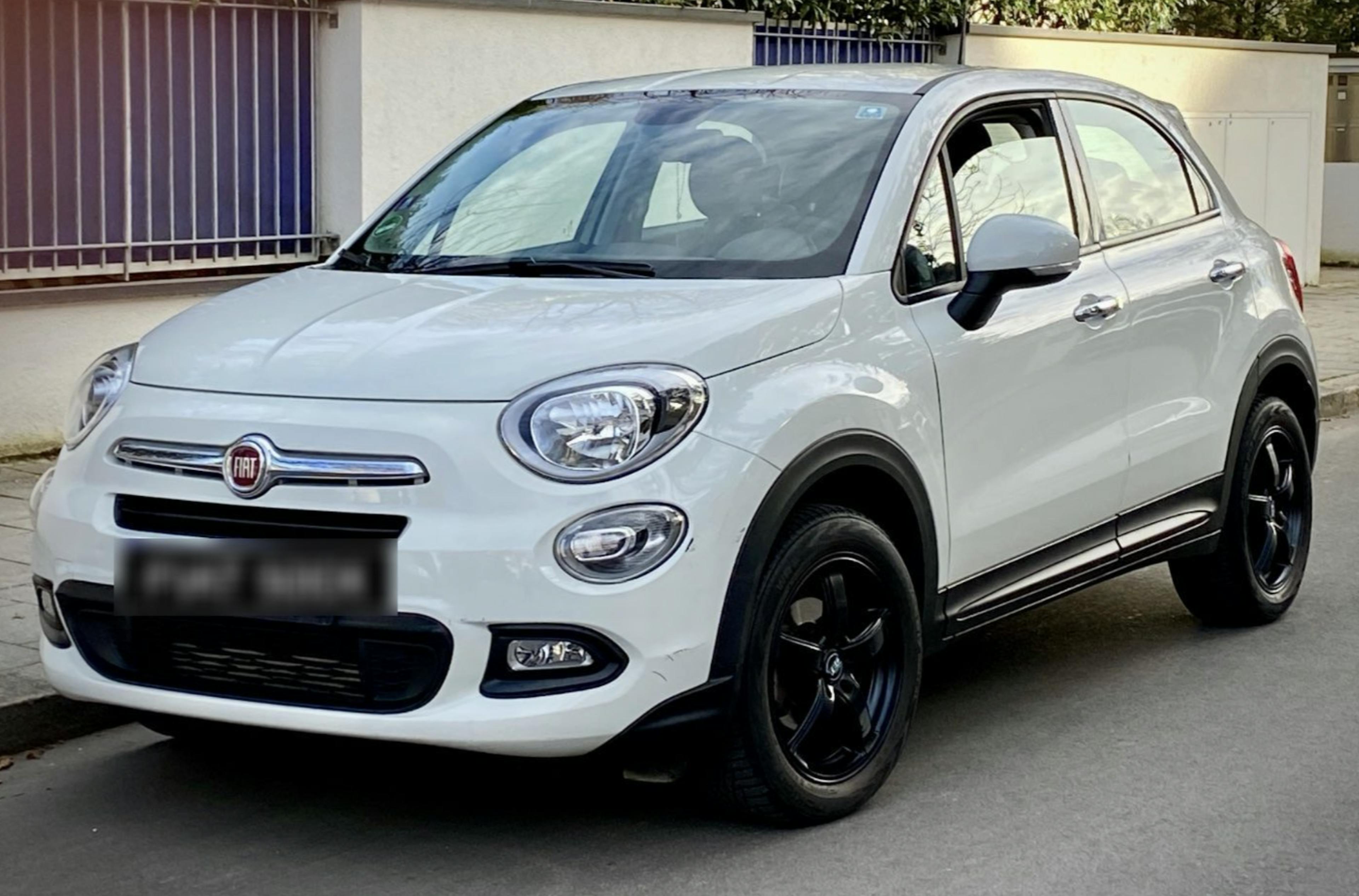 Weißer Fiat 500X am Straßenrand stehend vor einer weißen Mauer.
