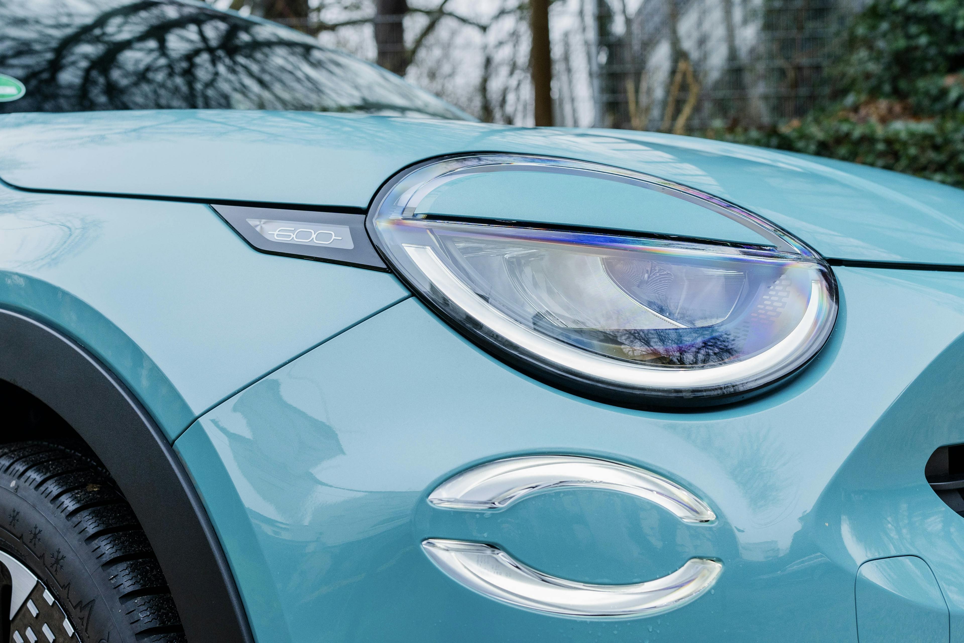 Detailansicht des Scheinwerfers eines grün-blauen Fiat 600 Hybrid.