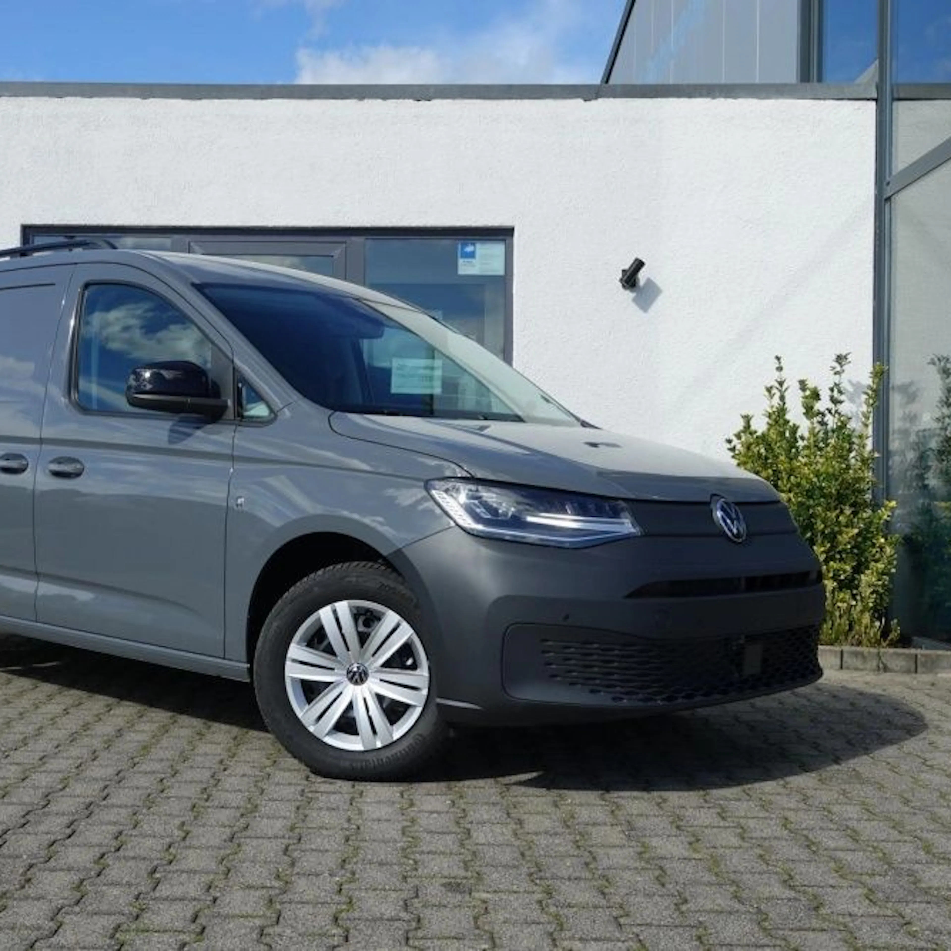 Ein grauer VW Caddy Cargo Maxi parkt auf einem Hof.