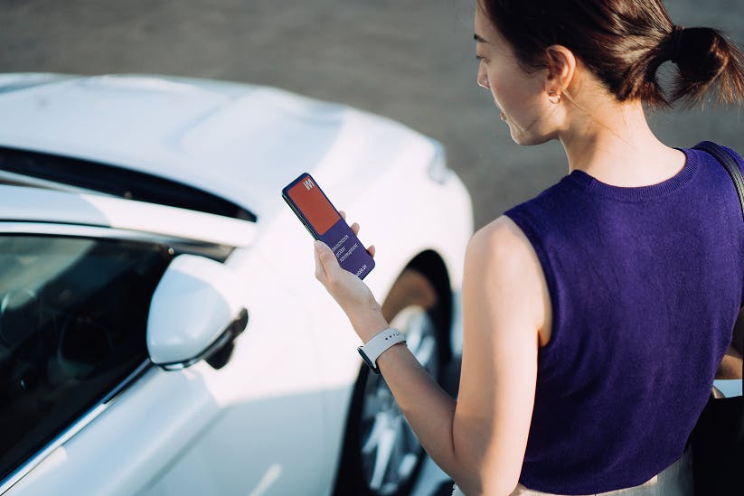 Eine Frau steht neben einem Auto und schaut auf ihr Smartphone