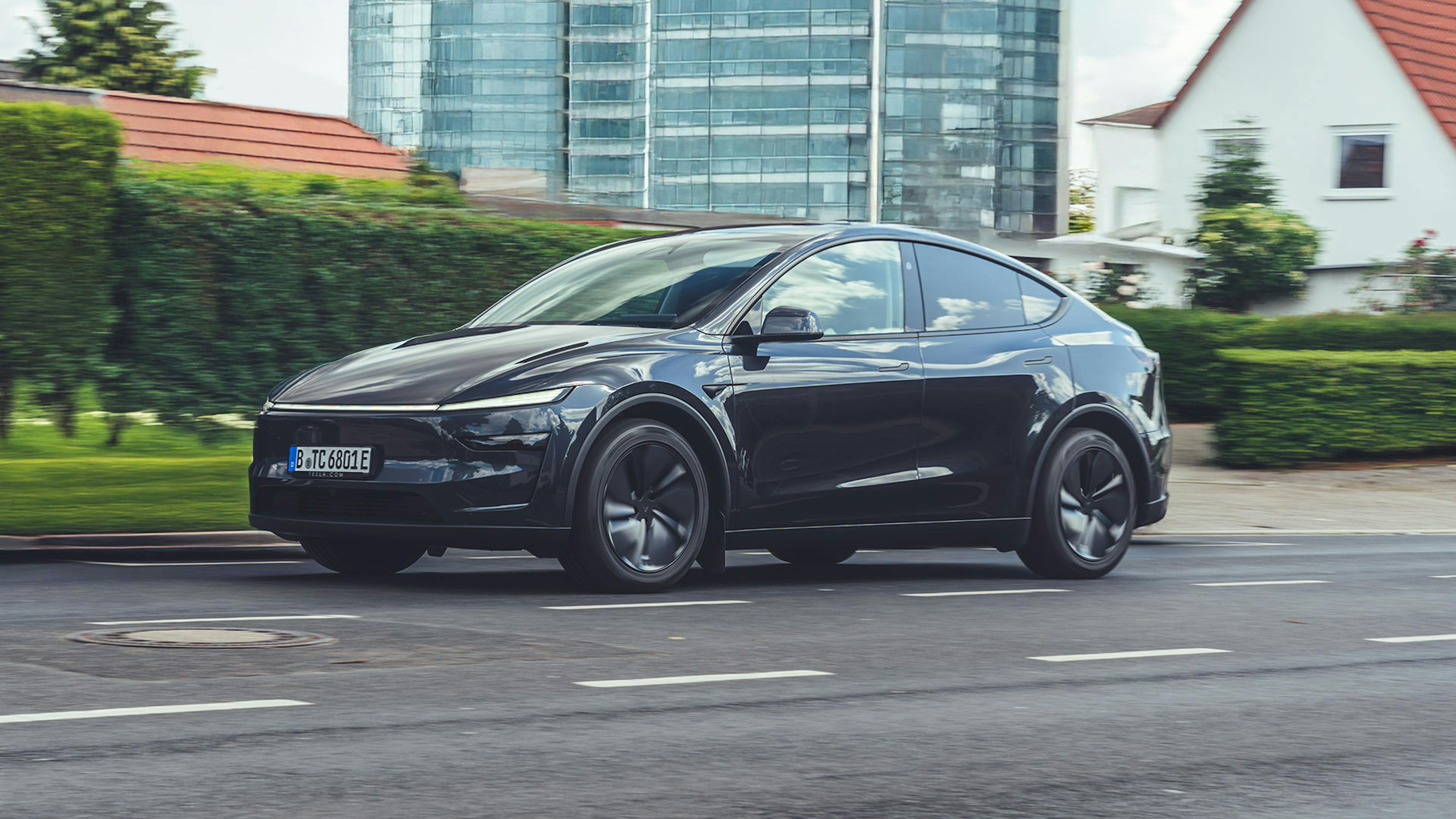 Ein dunkelgraues Tesla Model Y fährt in einer Großstadt eine Straße entlang