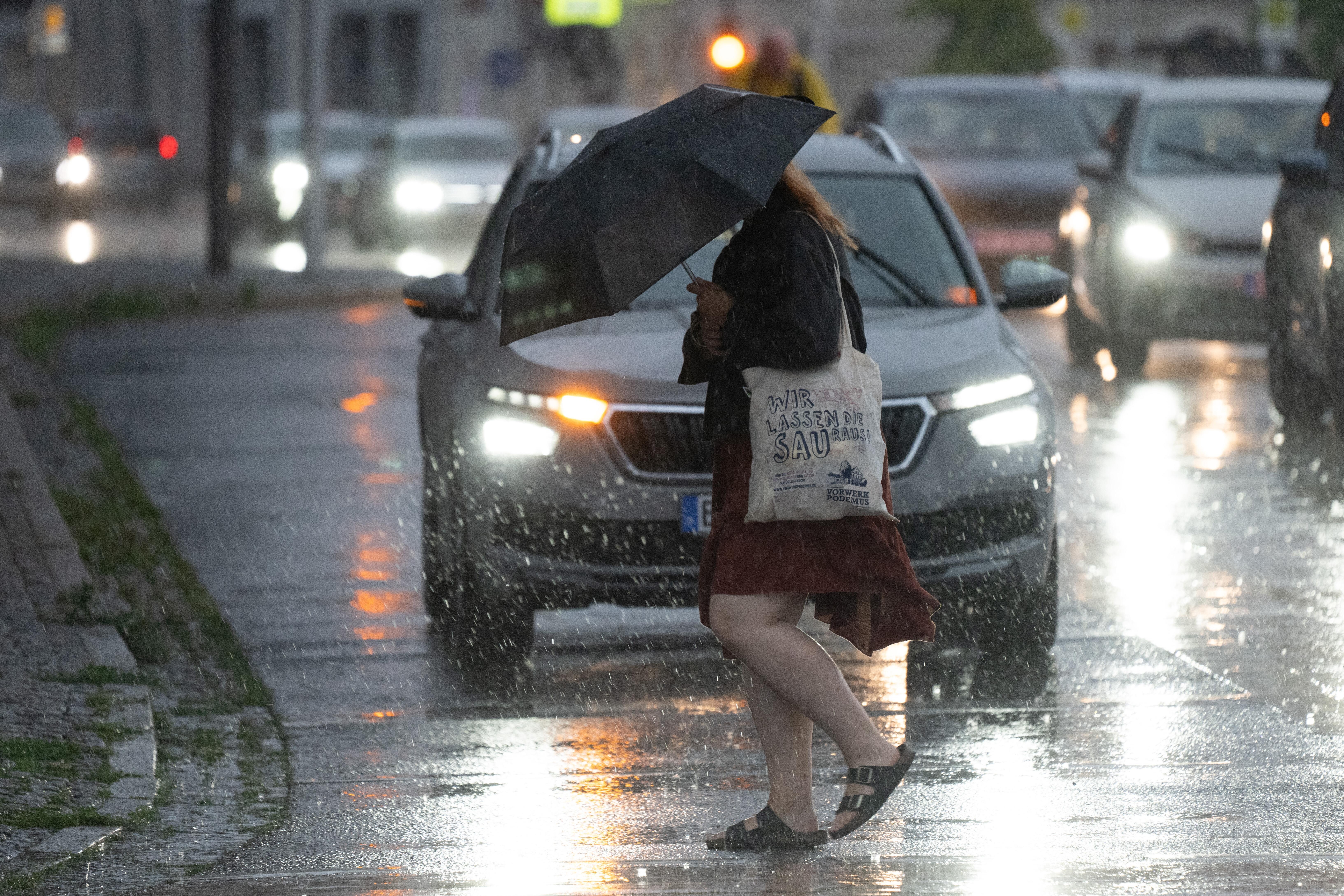 Eine Passantin überquert bei starkem Regen eine Straße mit einem Regenschirm.