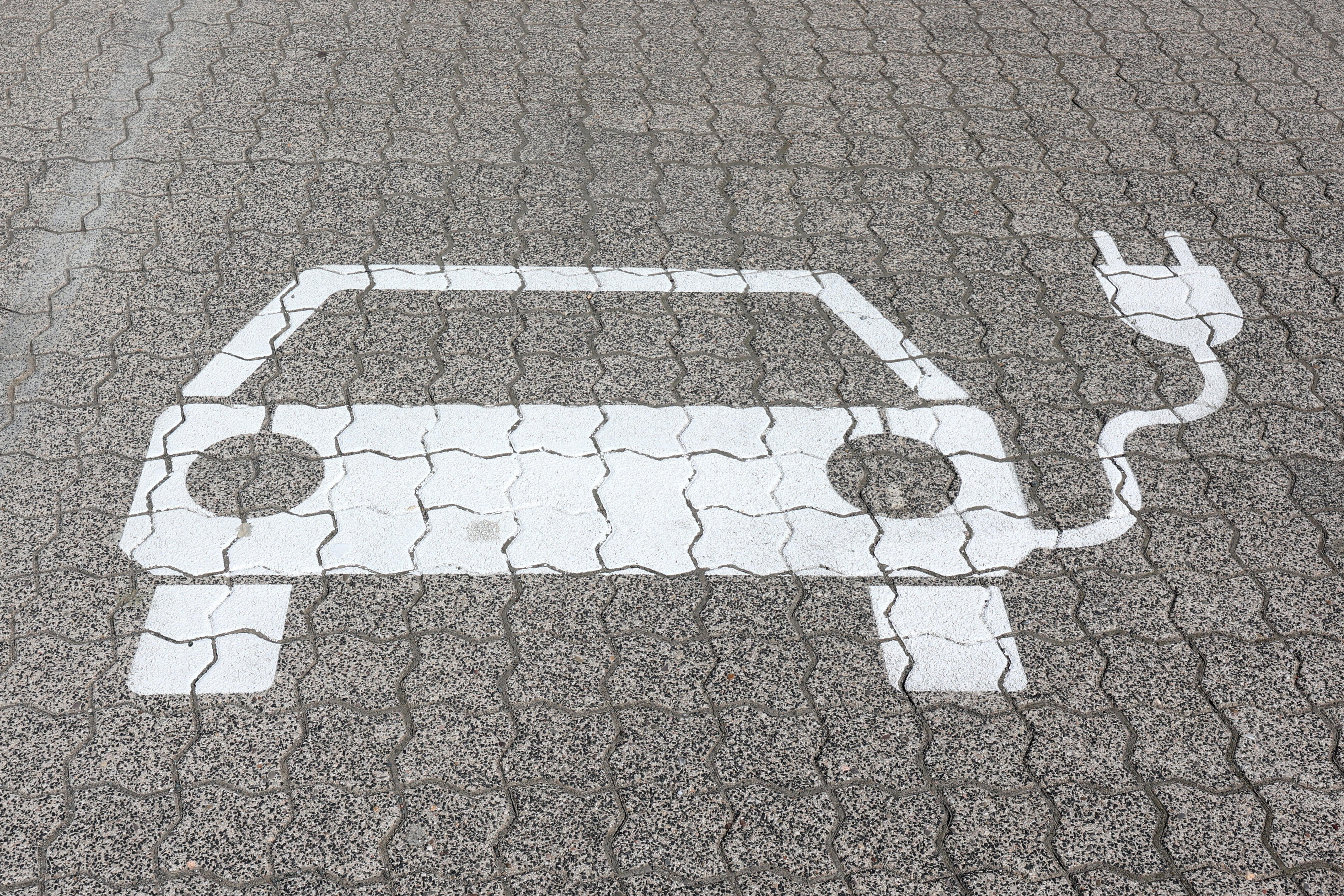 Ein Piktogramm eines E-Autos ist mit weißer Farbe auf den gepflasterten Weg gemalt.
