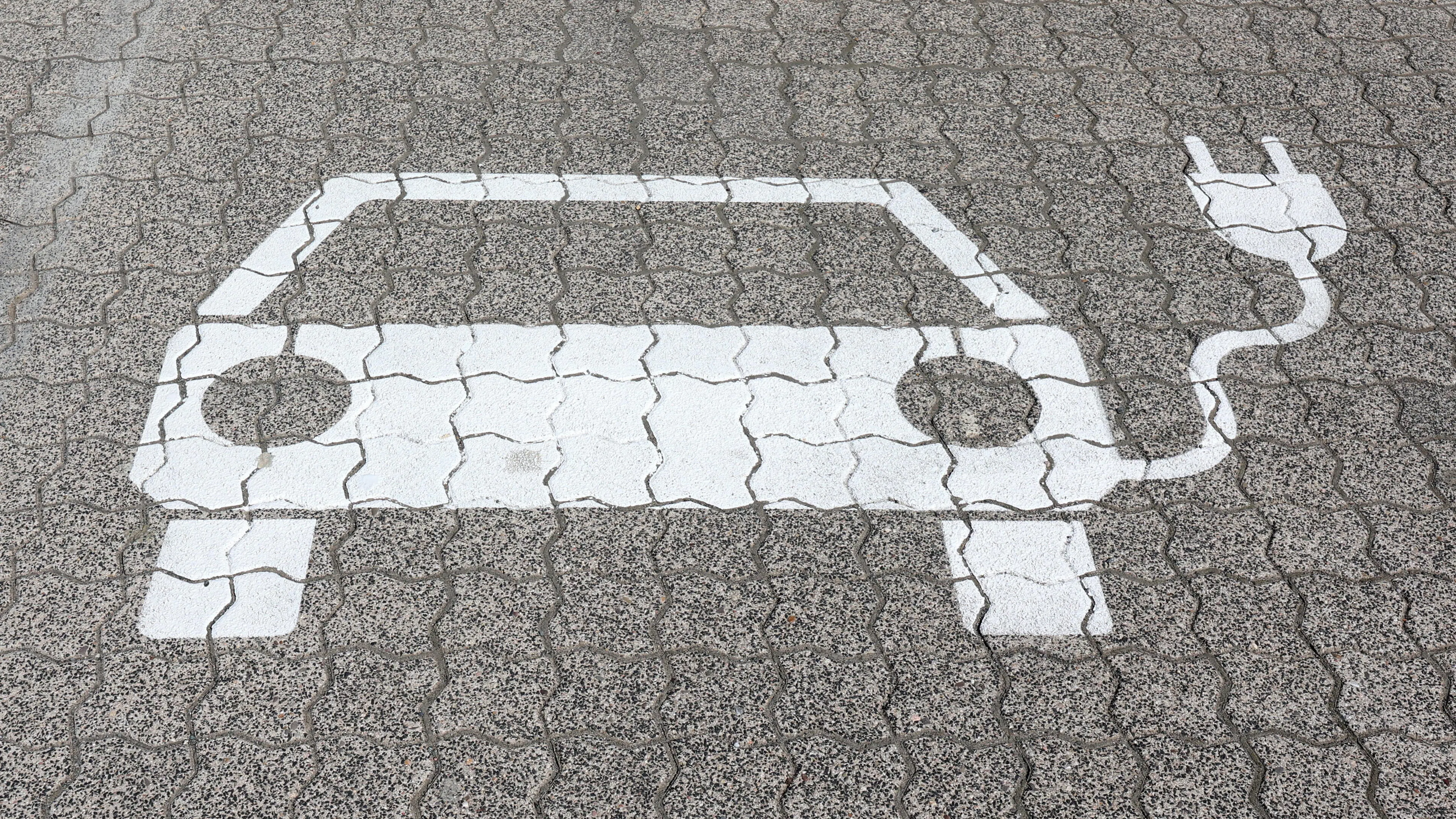 Ein Piktogramm eines E-Autos ist mit weißer Farbe auf den gepflasterten Weg gemalt.