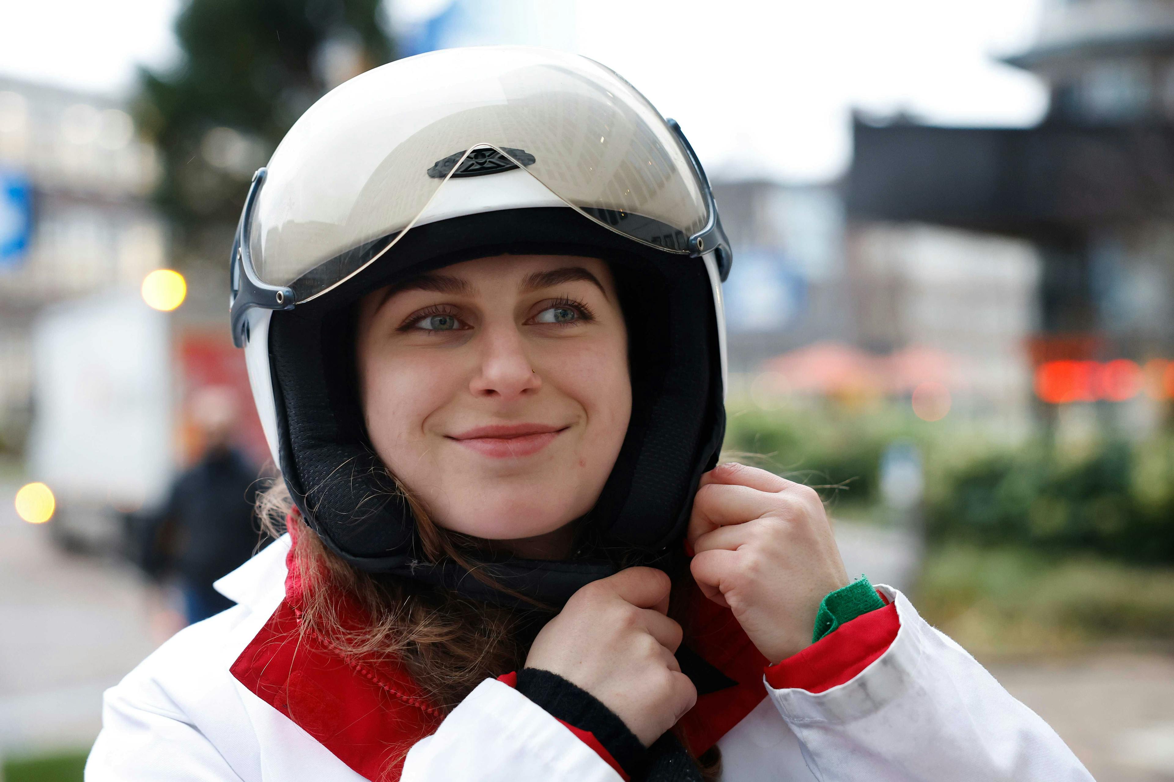 Eine Person trägt eine weiße Jacke mit roten Details und setzt sich einen Motorradhelm auf.