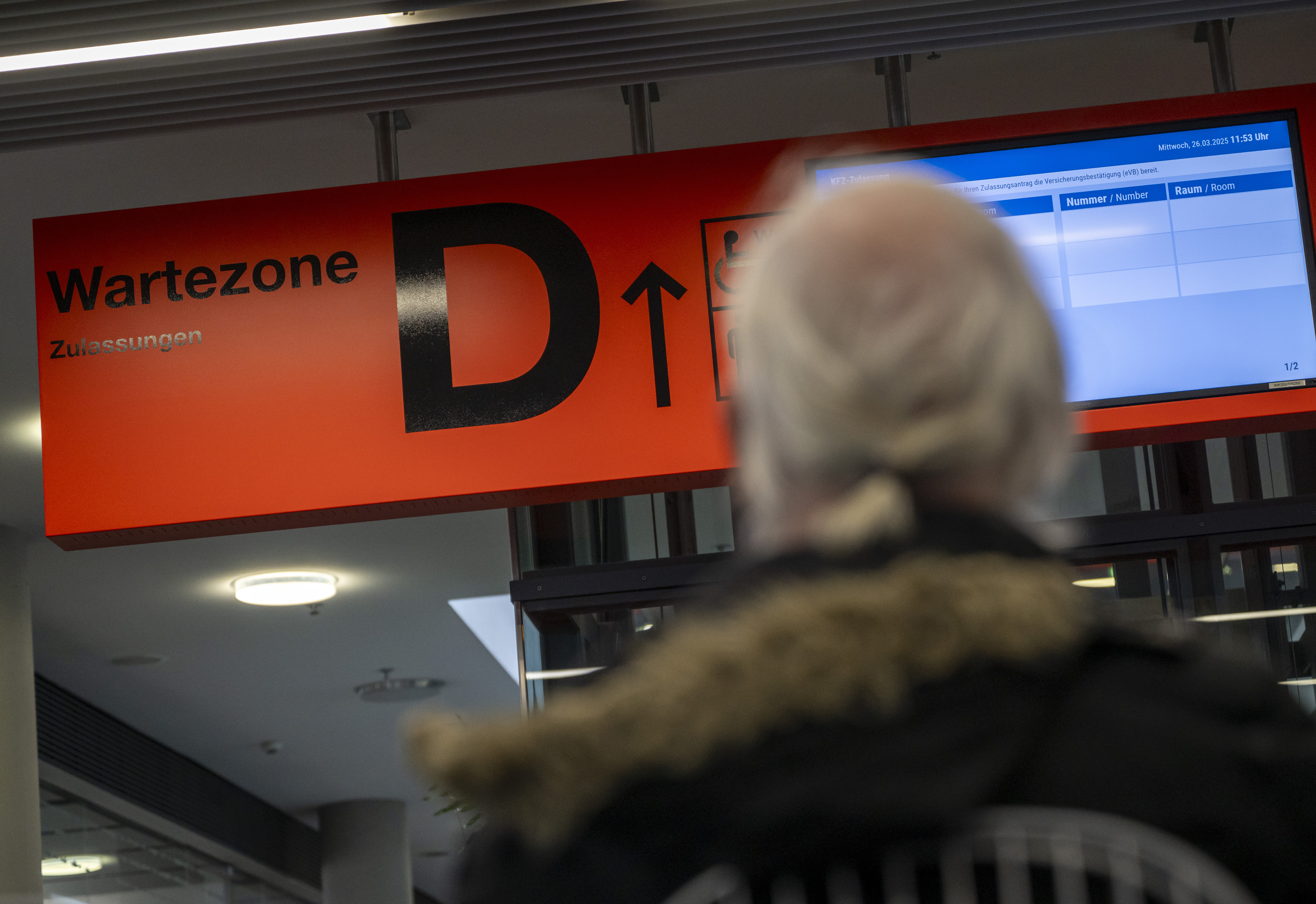 Ein Mann schaut auf ein rotes Schild mit schwarzer Aufschrift: Wartezone D.