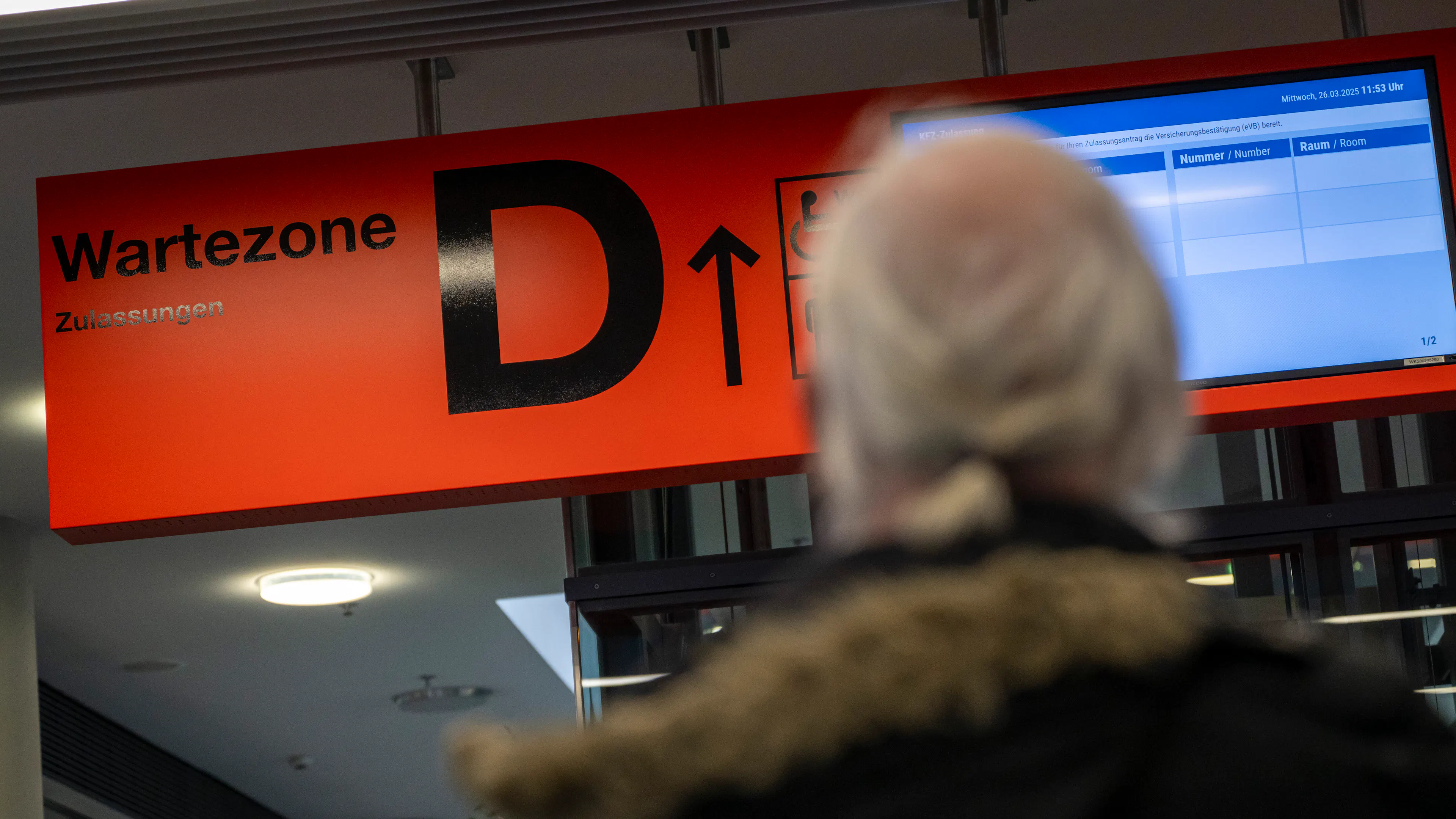 Ein Mann schaut auf ein rotes Schild mit schwarzer Aufschrift: Wartezone D.