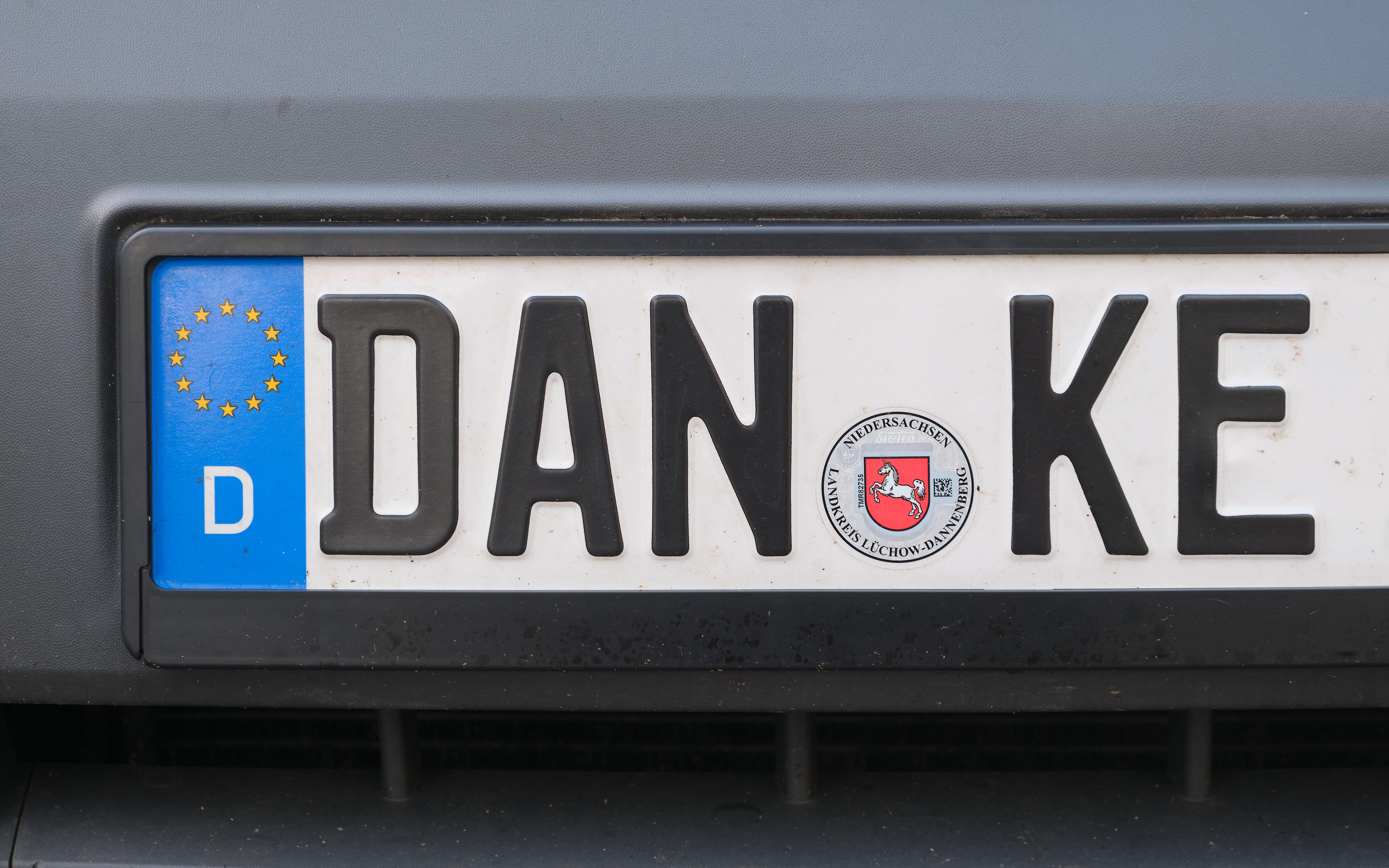 An einem dunkelgrauen Auto ist ein Kennzeichen mit der Buchstabenkombination DAN-KE befestigt.