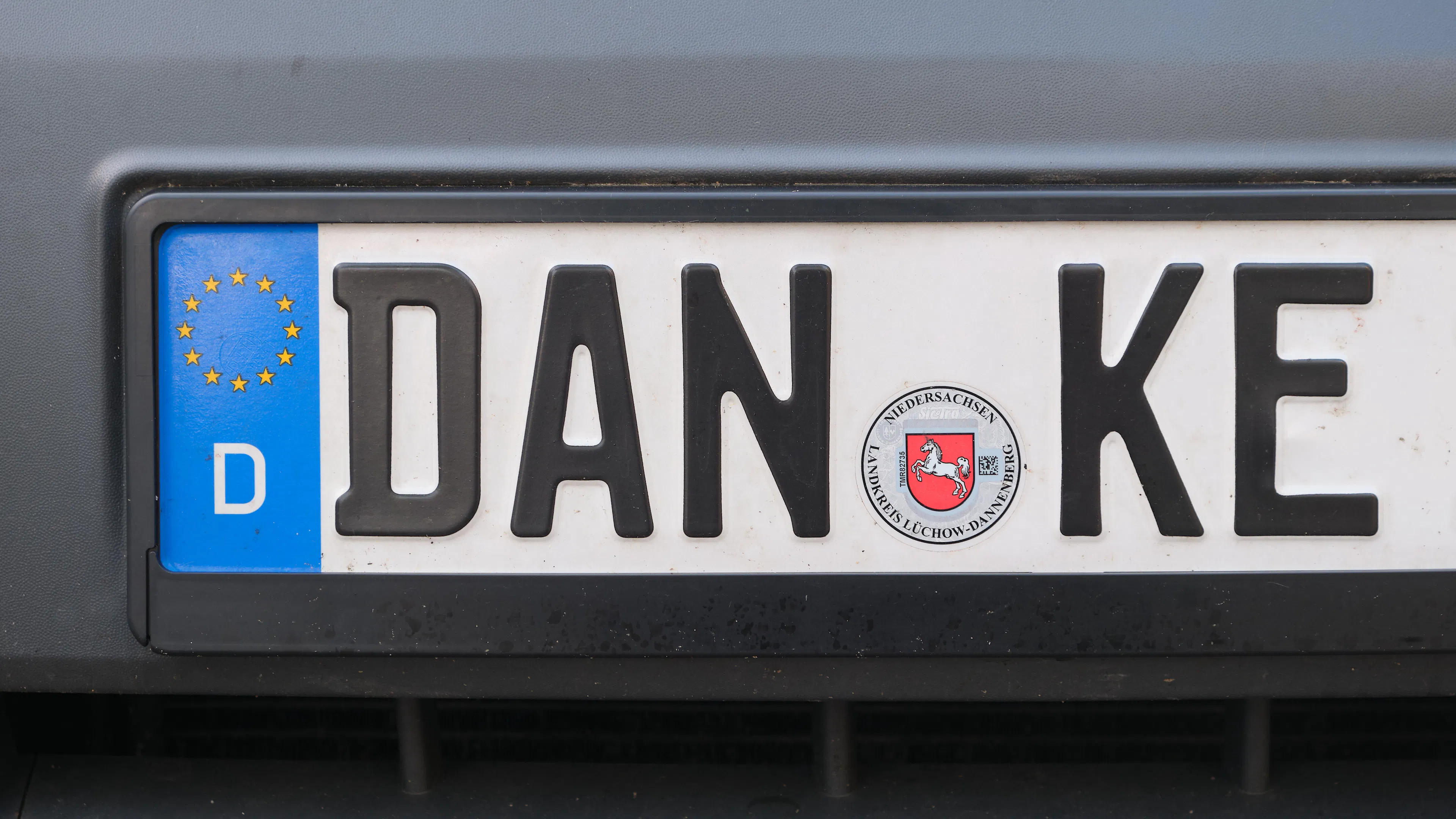 An einem dunkelgrauen Auto ist ein Kennzeichen mit der Buchstabenkombination DAN-KE befestigt.
