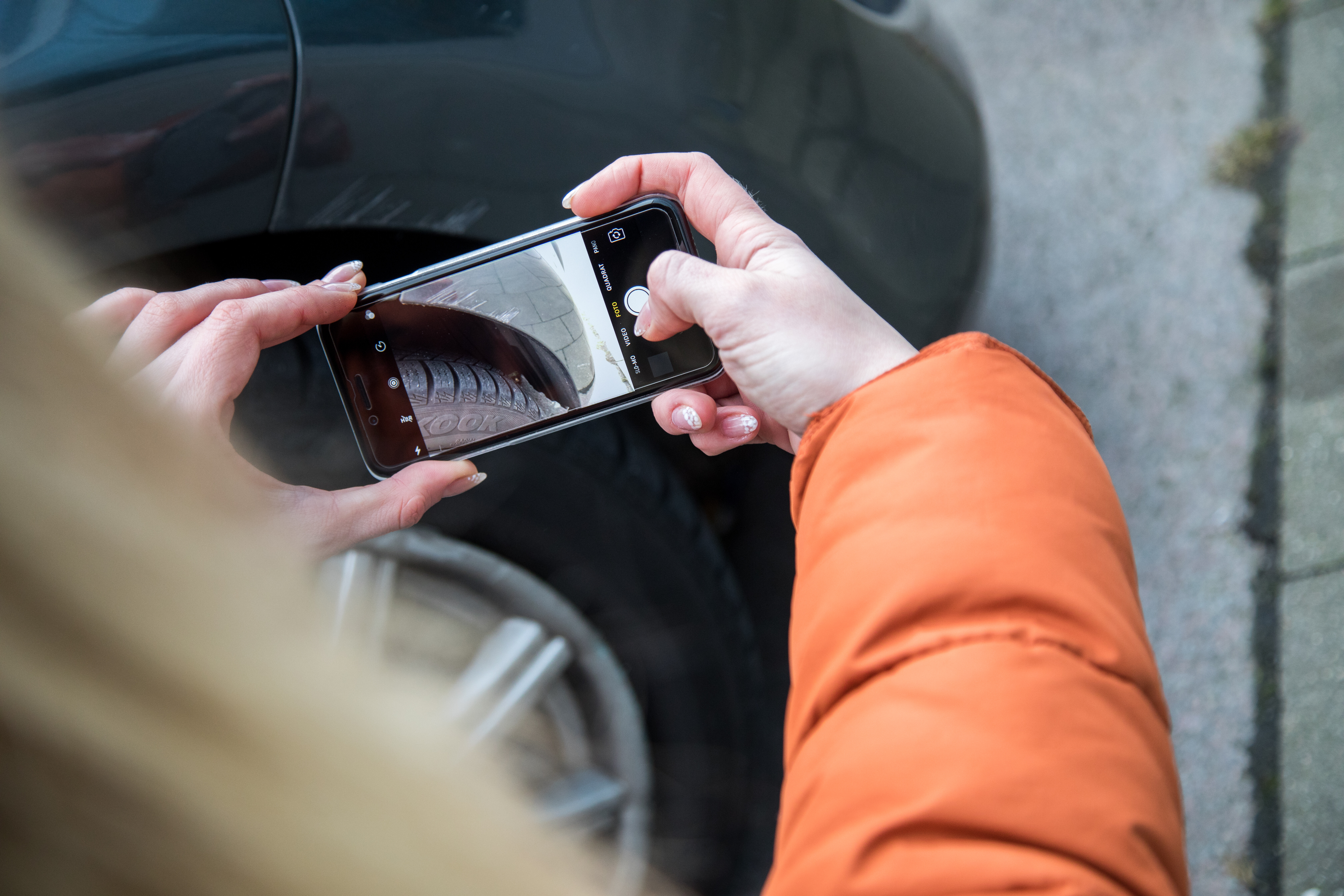 Eine Frau fotografiert mit dem Handy Schäden an einem Fahrzeug.