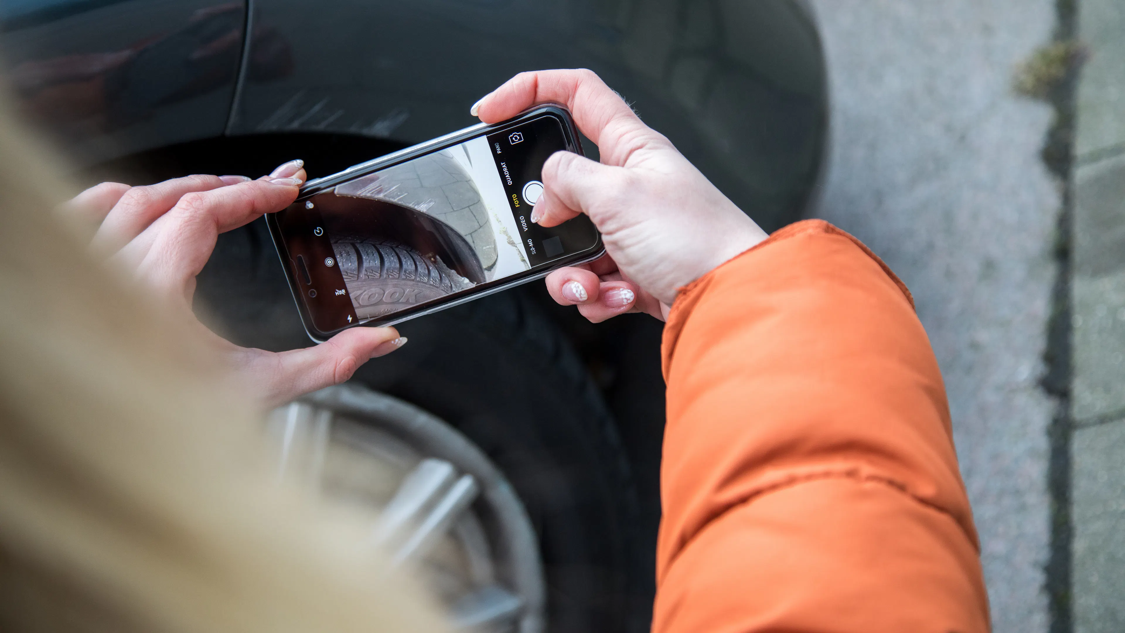 Eine Frau fotografiert mit dem Handy Schäden an einem Fahrzeug.
