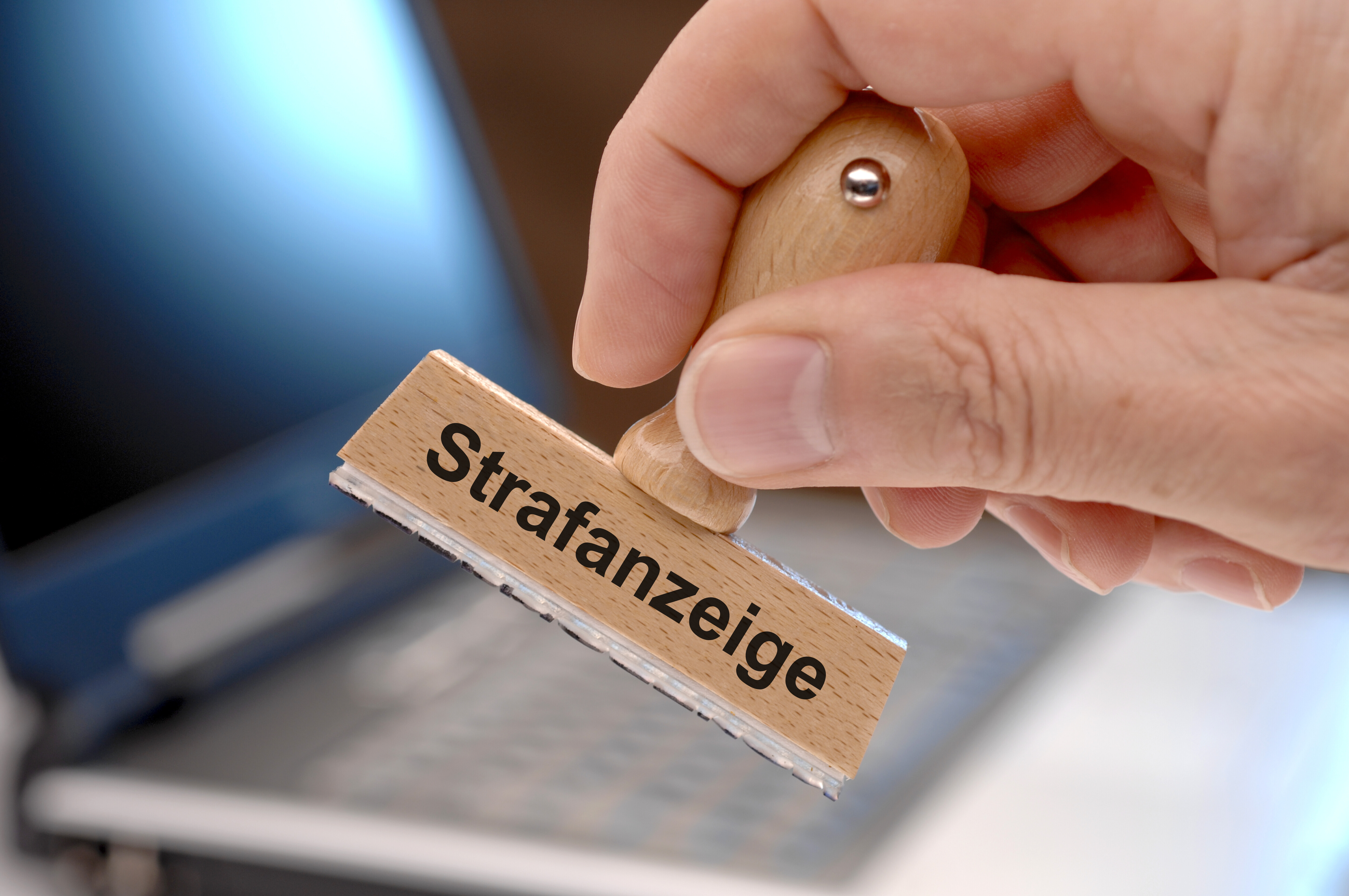 Jemand hält einen Holzstempel in der Hand. Darauf steht in schwarzer Schrift: "Strafanzeige".