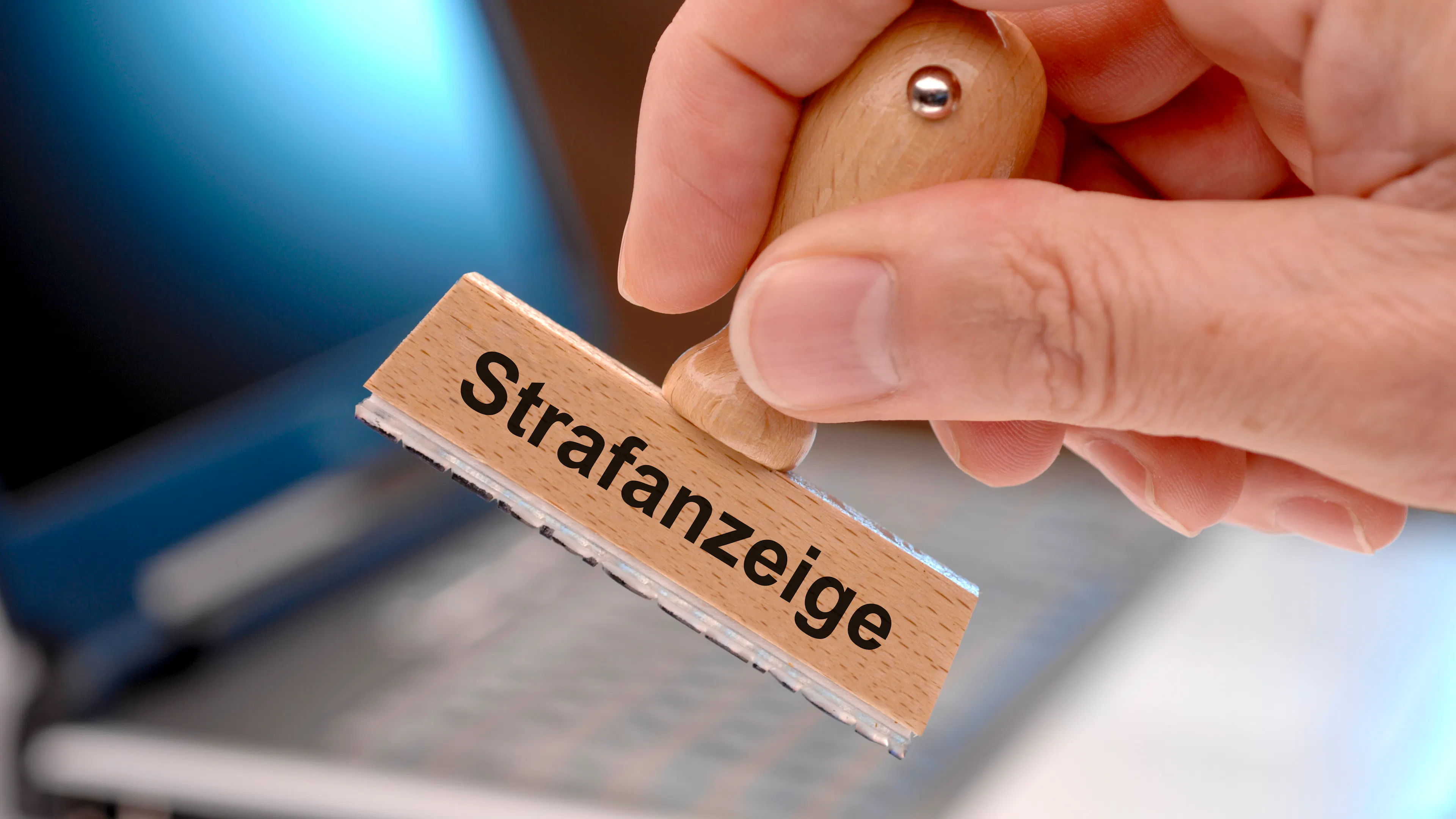 Jemand hält einen Holzstempel in der Hand. Darauf steht in schwarzer Schrift: "Strafanzeige".