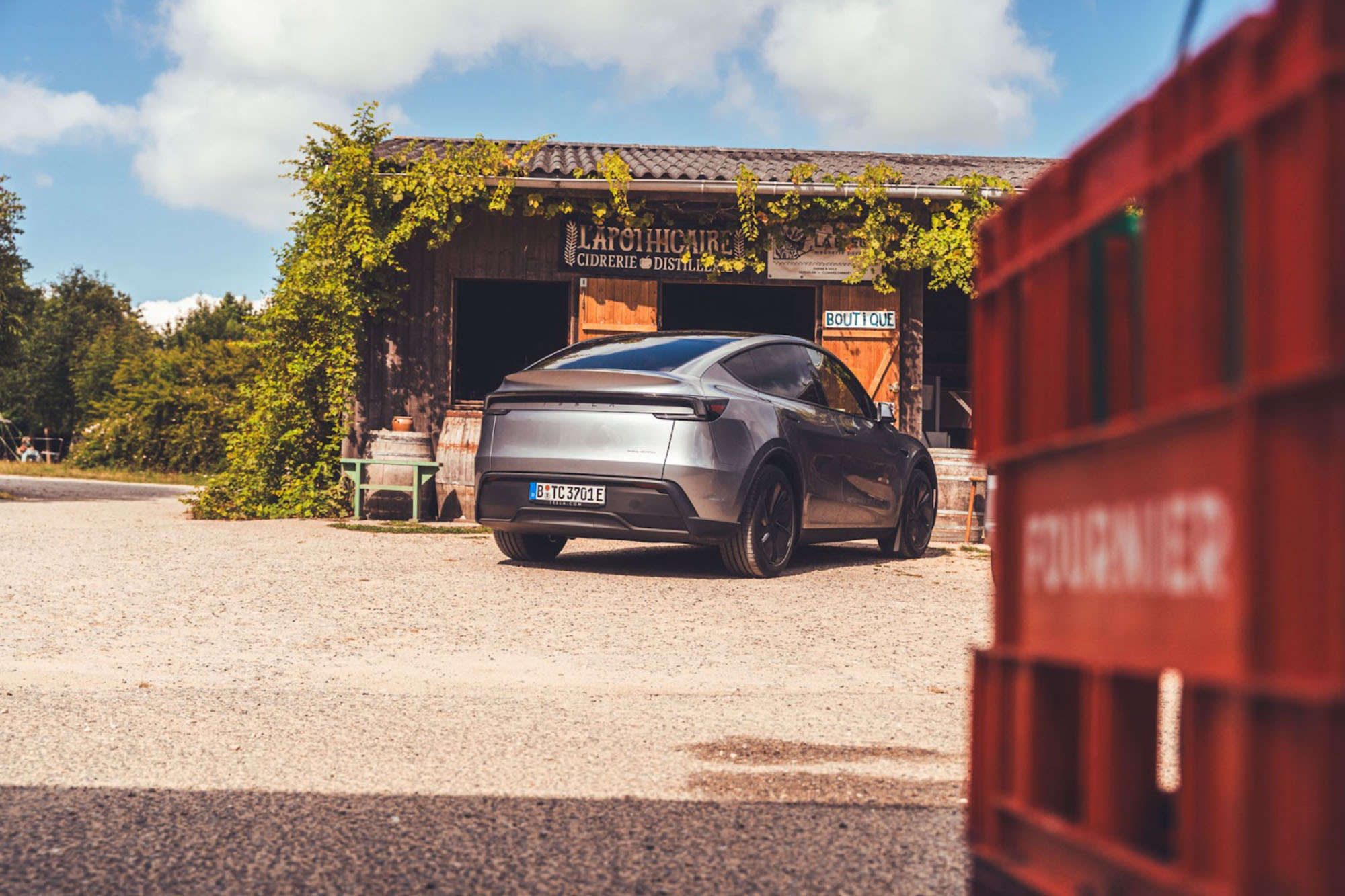 Ein dunkelgraues Tesla Model Y parkt vor einem landwirtschaftlichen Gebäude
