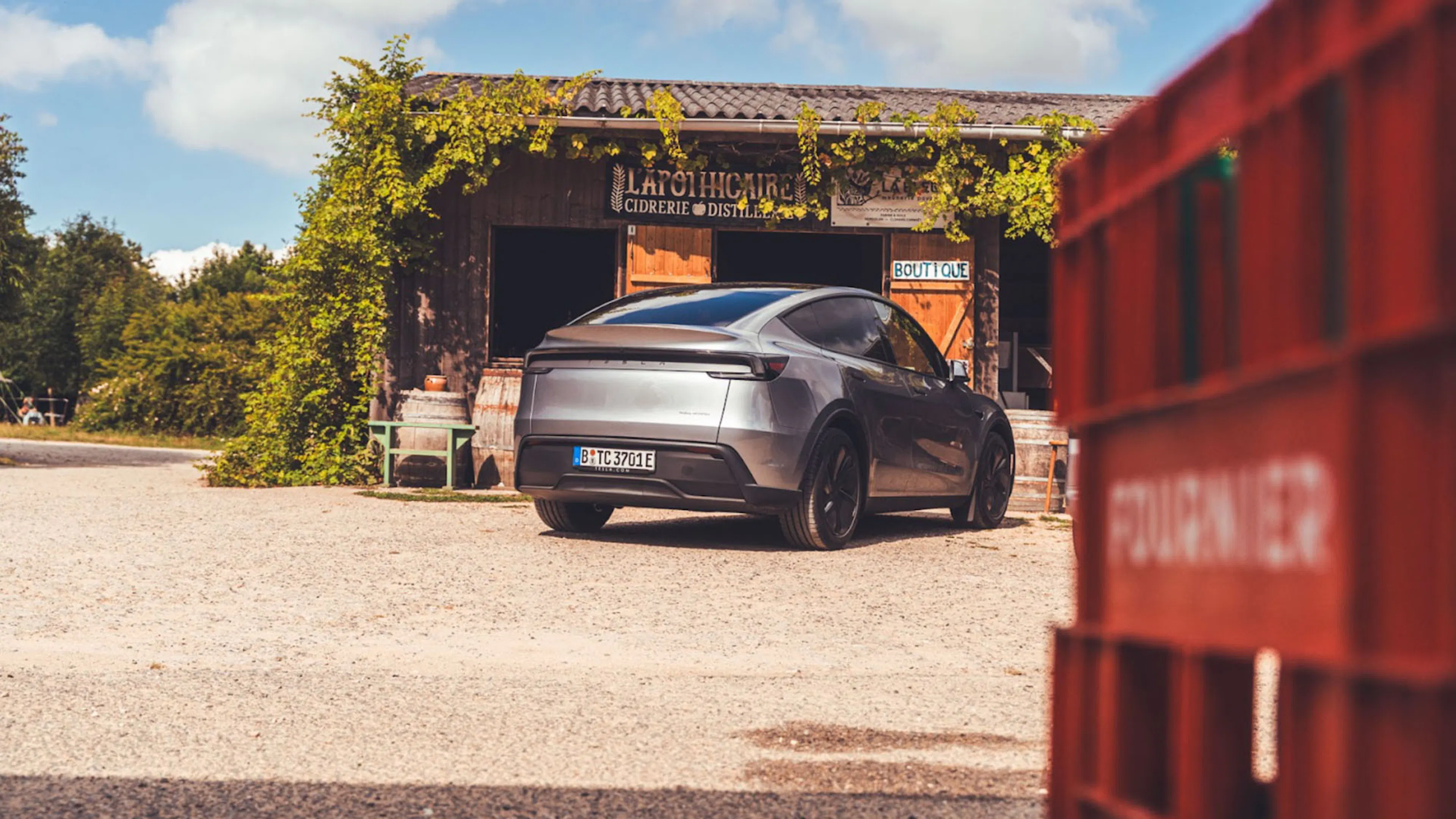 Ein dunkelgraues Tesla Model Y parkt vor einem landwirtschaftlichen Gebäude