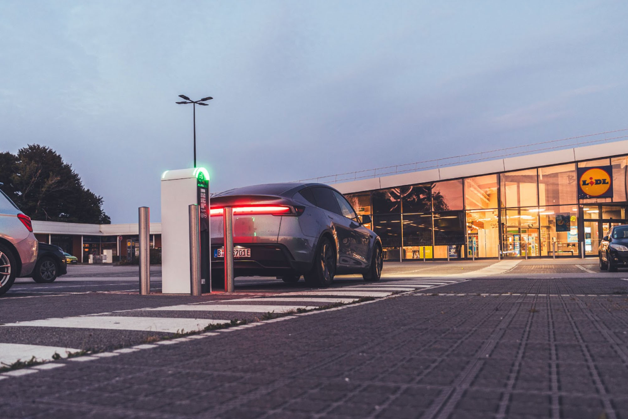 Ein dunkelgraues Tesla Model Y parkt vor einem Supermarkt an einer Ladesäule