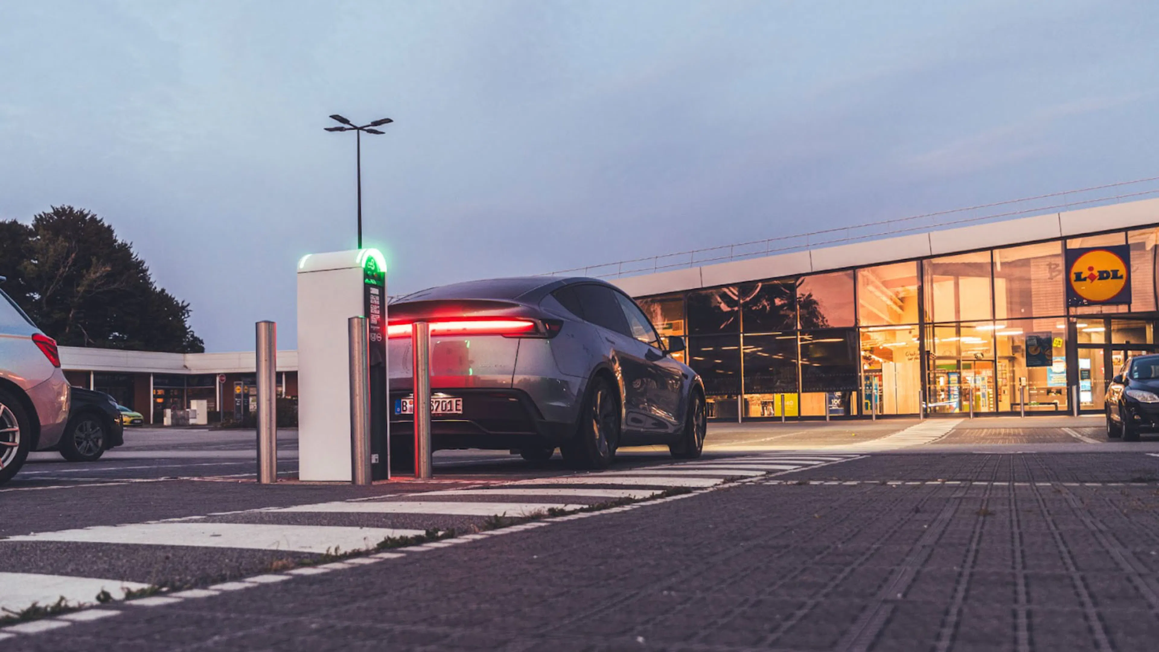 Ein dunkelgraues Tesla Model Y parkt vor einem Supermarkt an einer Ladesäule