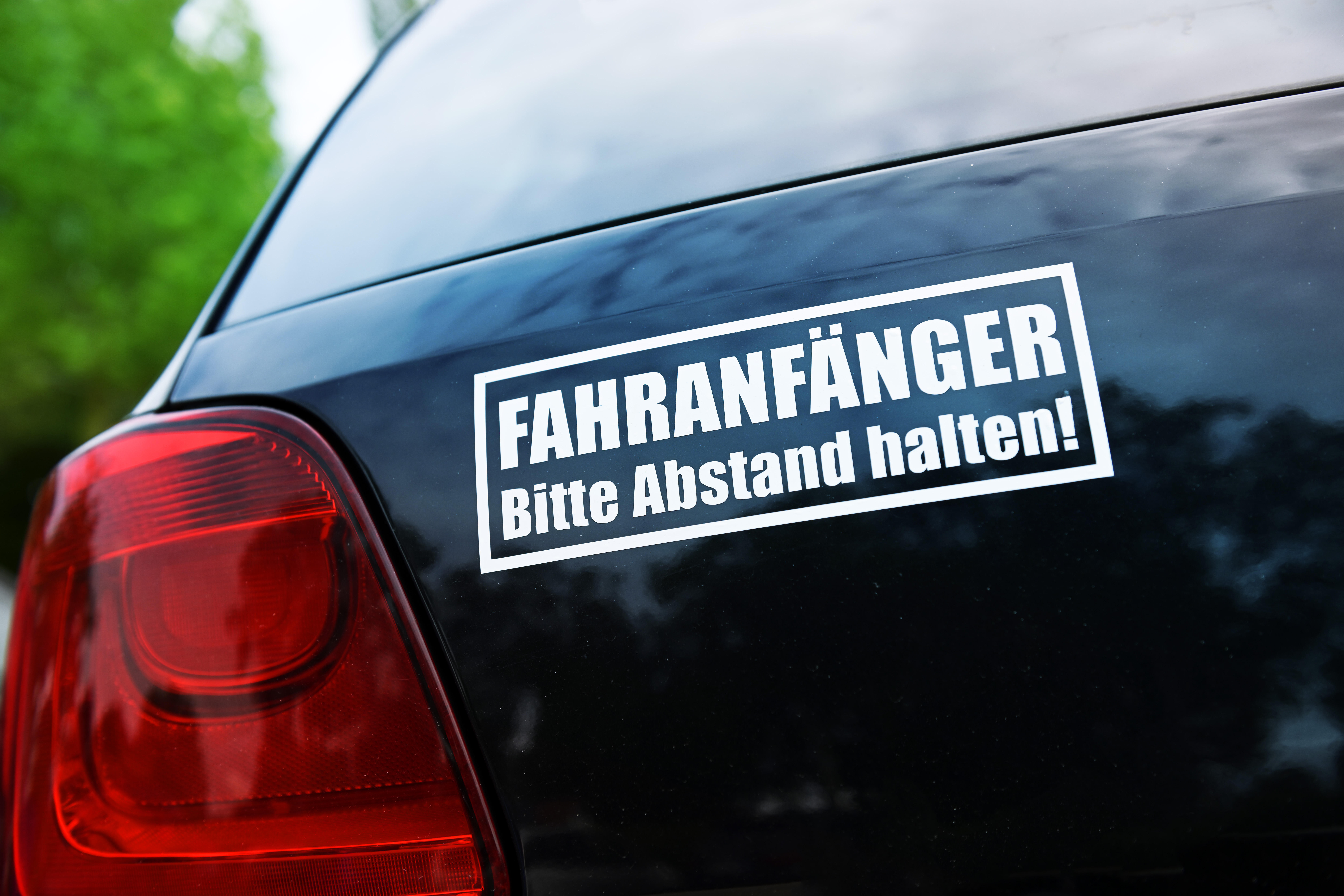 Schwarzes Auto mit einem auffälliger Aufkleber mit der Aufschrift „FAHRANFÄNGER – Bitte Abstand halten!“.