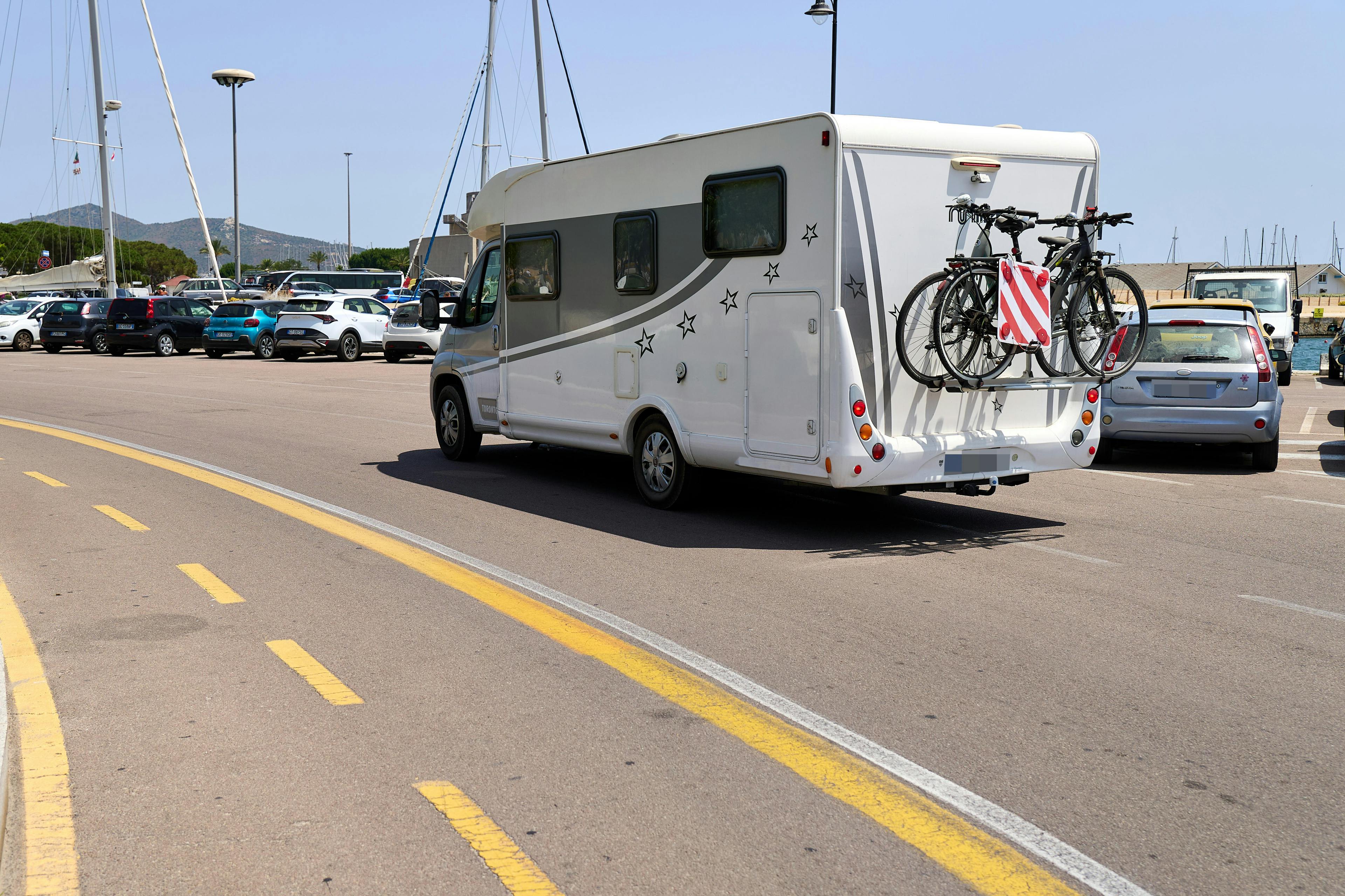 Ein Wohnmobil mit Fahrradträger fährt im Sommer über den Parkplatz von Olbia auf Sardinien