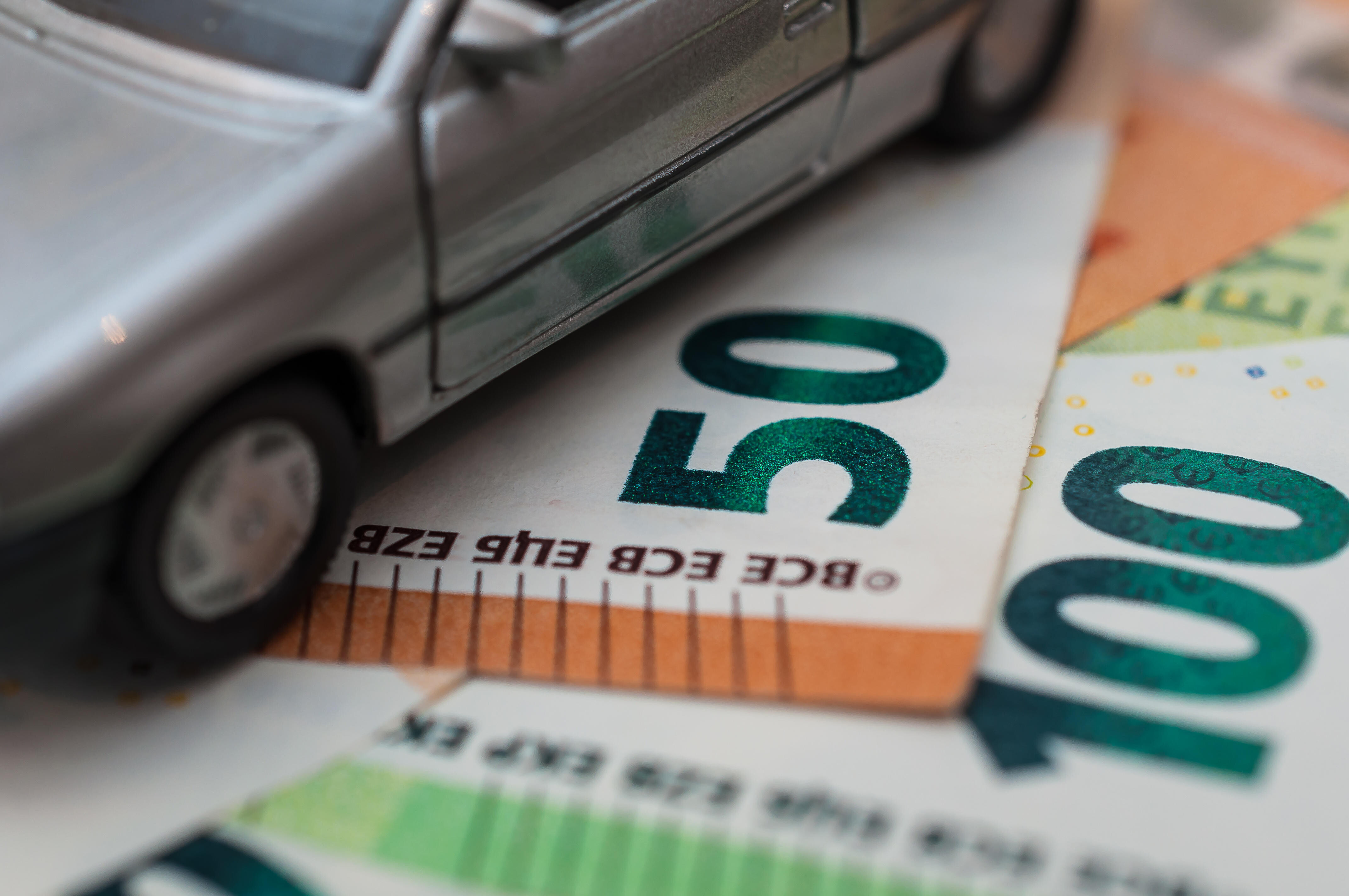 Ein Spielzeugauto steht auf Euro-Geldscheinen.