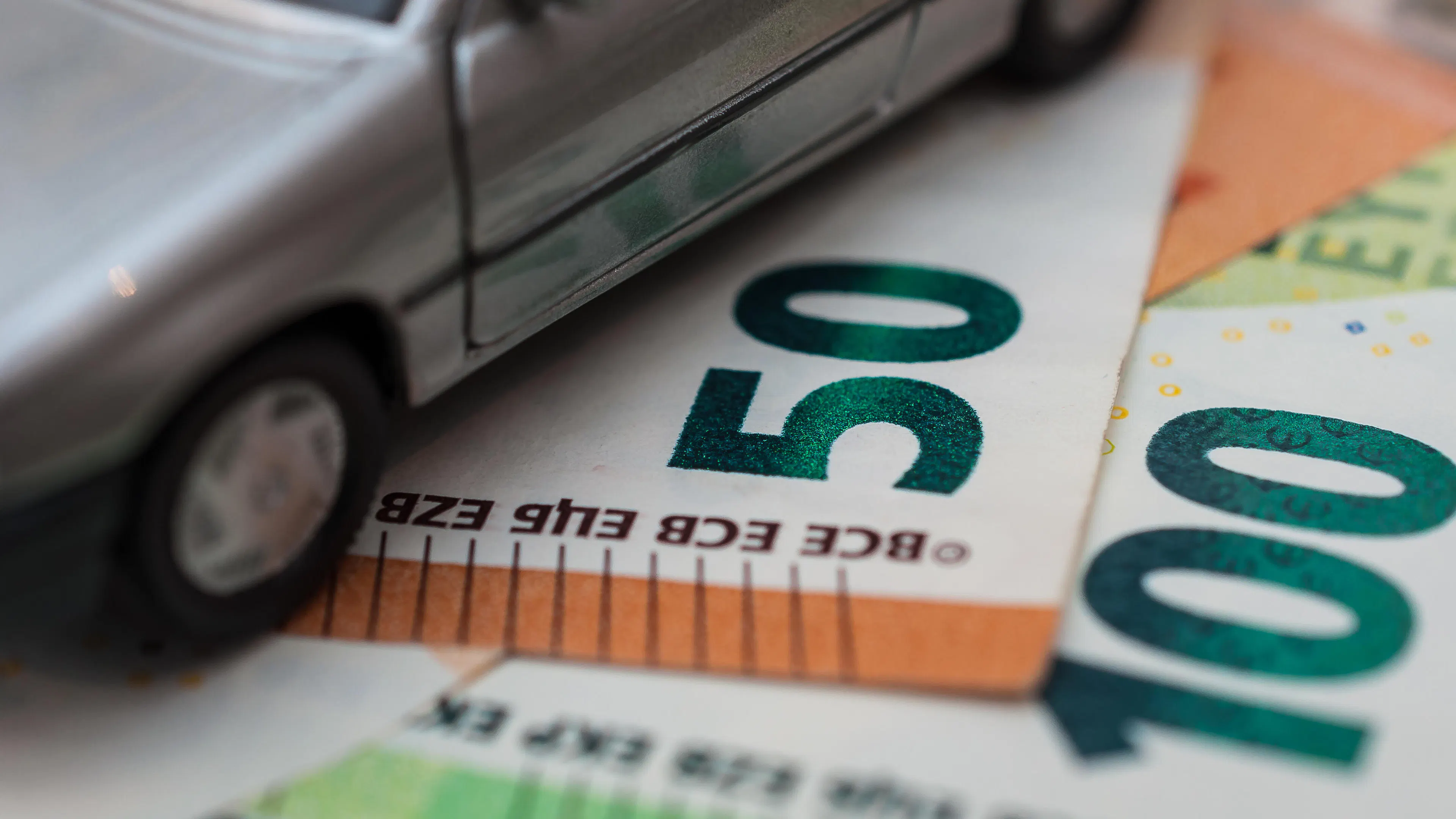 Ein Spielzeugauto steht auf Euro-Geldscheinen.