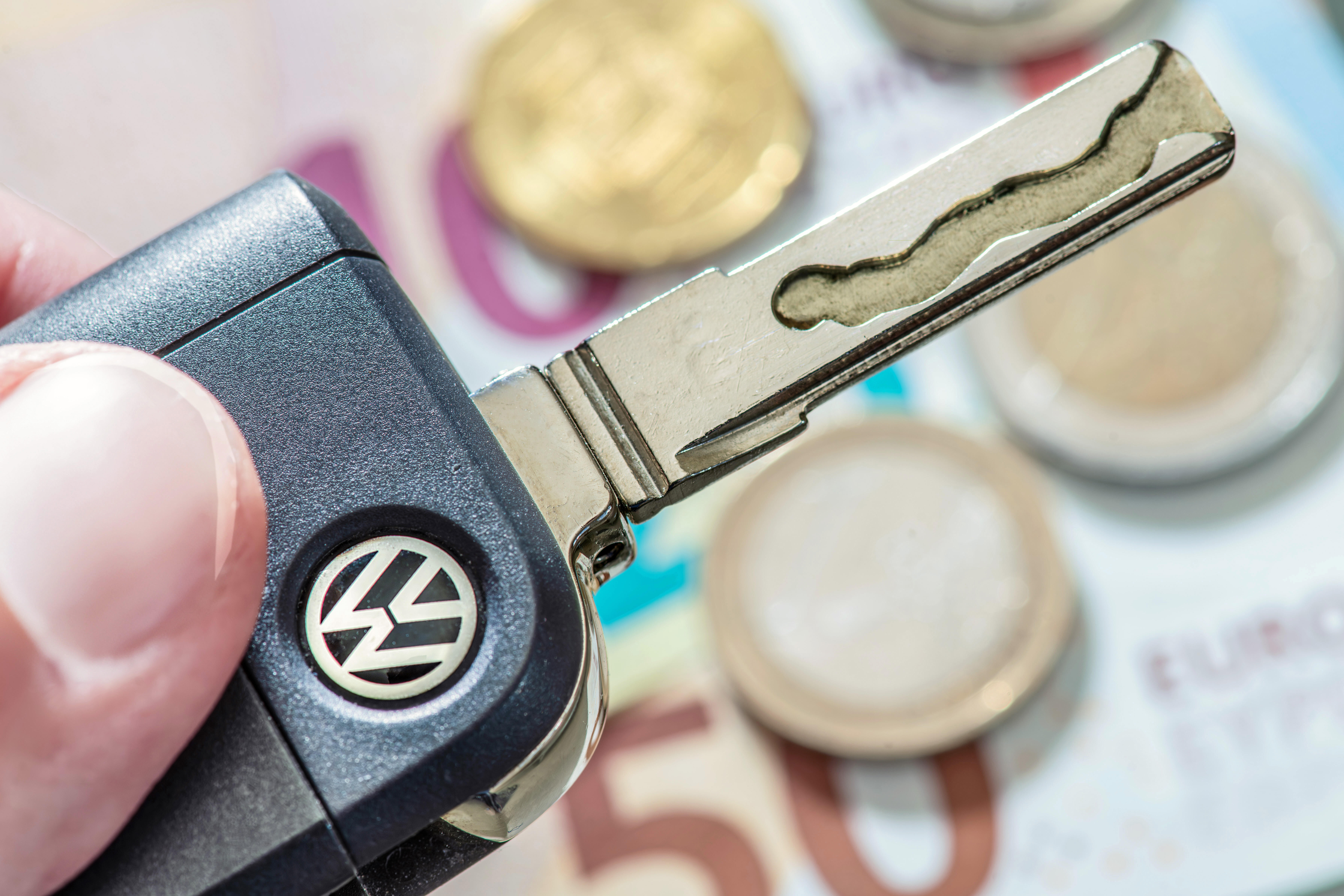 Jemand hält einen Autoschlüssel von VW in der Hand. Im Hintergrund sieht man Geldscheine und Münzen.