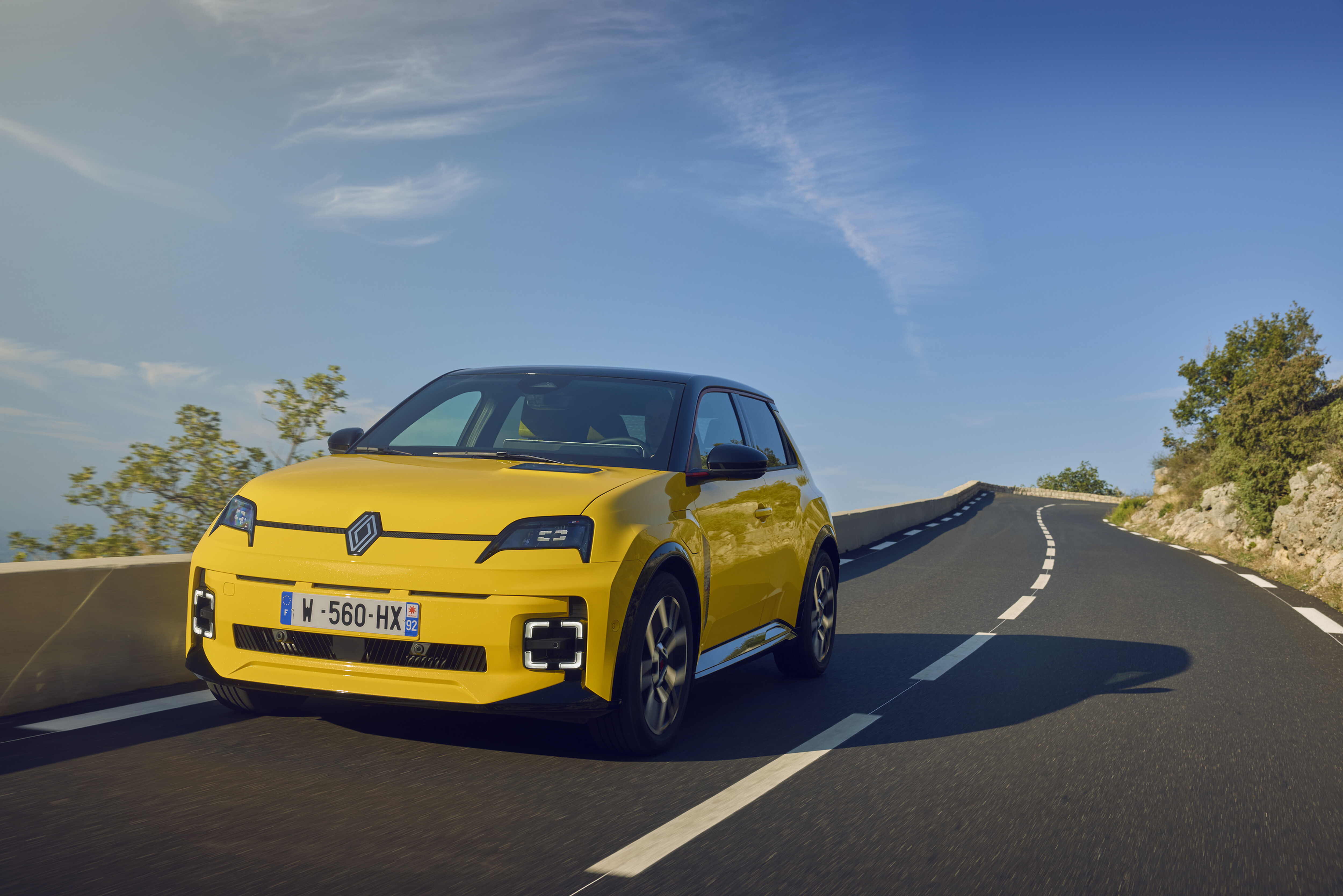Gelber Renault 5 E-Tech fährt auf einer Landstraße