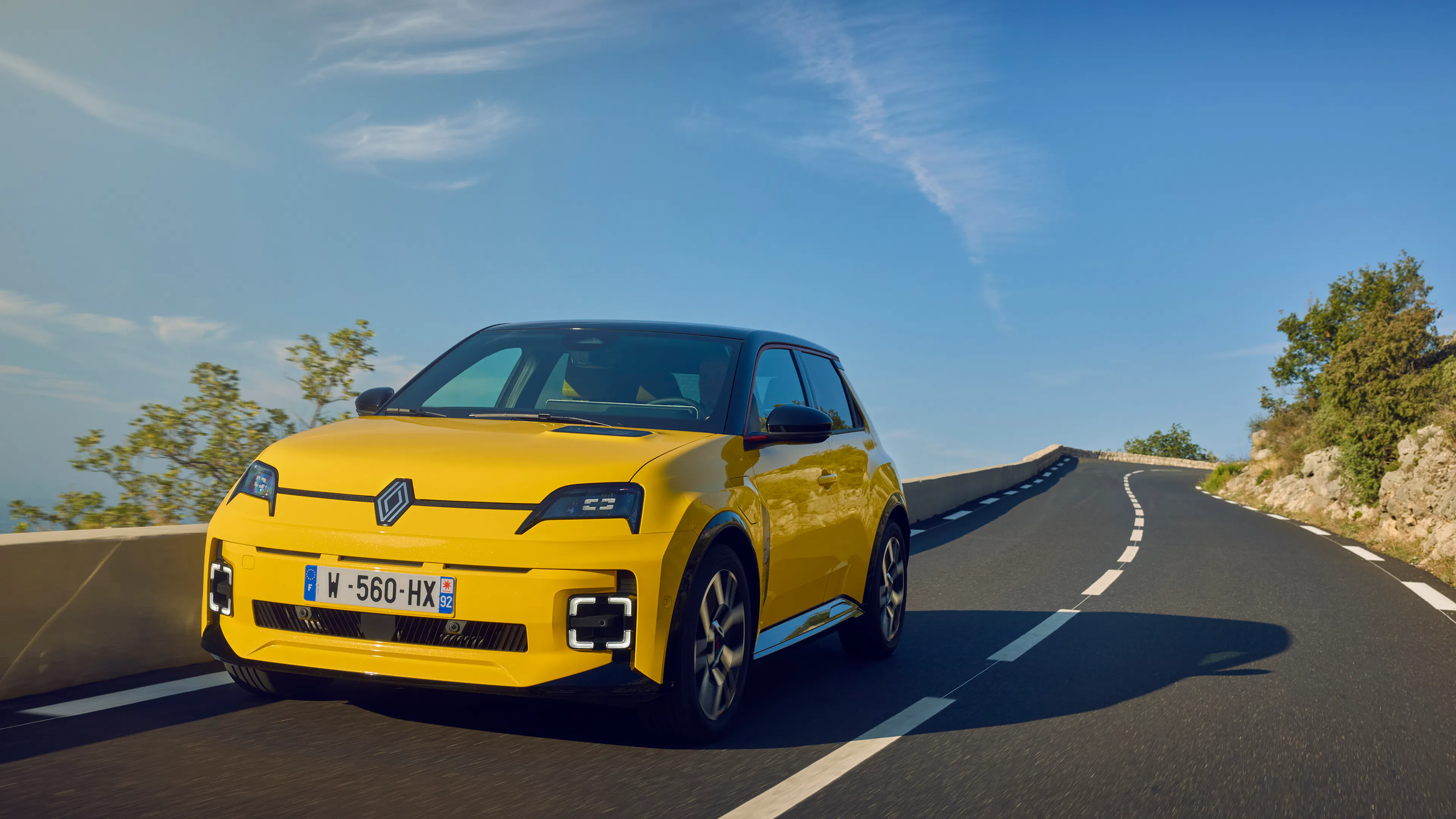 Gelber Renault 5 E-Tech fährt auf einer Landstraße