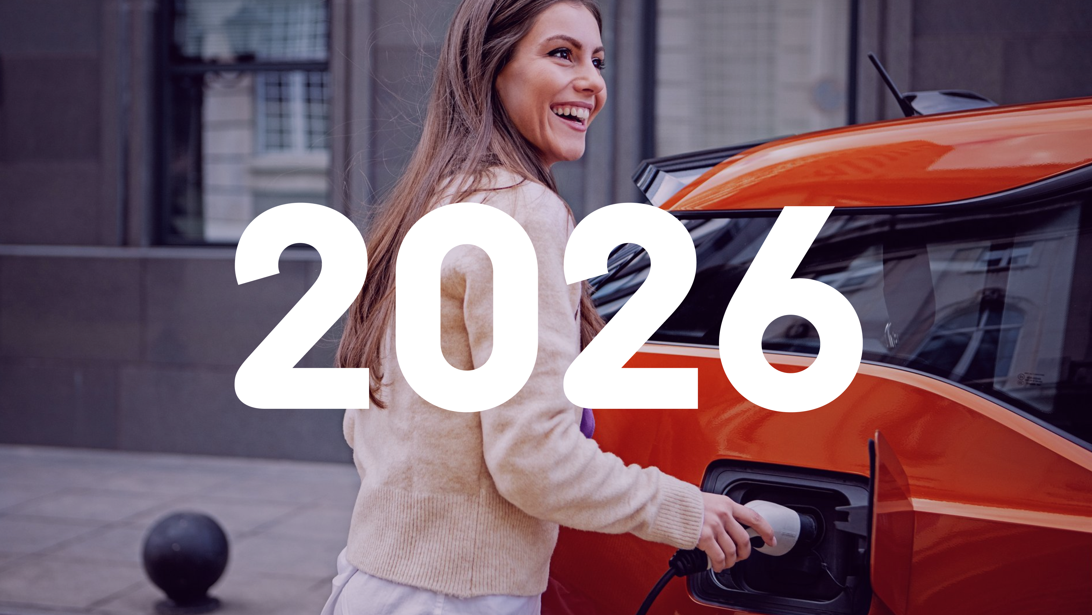 Eine junge Frau schließt ihr rotes Elektroauto an die Ladesäule an.