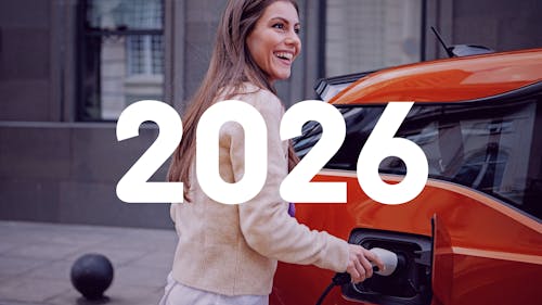 Eine junge Frau schließt ihr rotes Elektroauto an die Ladesäule an.