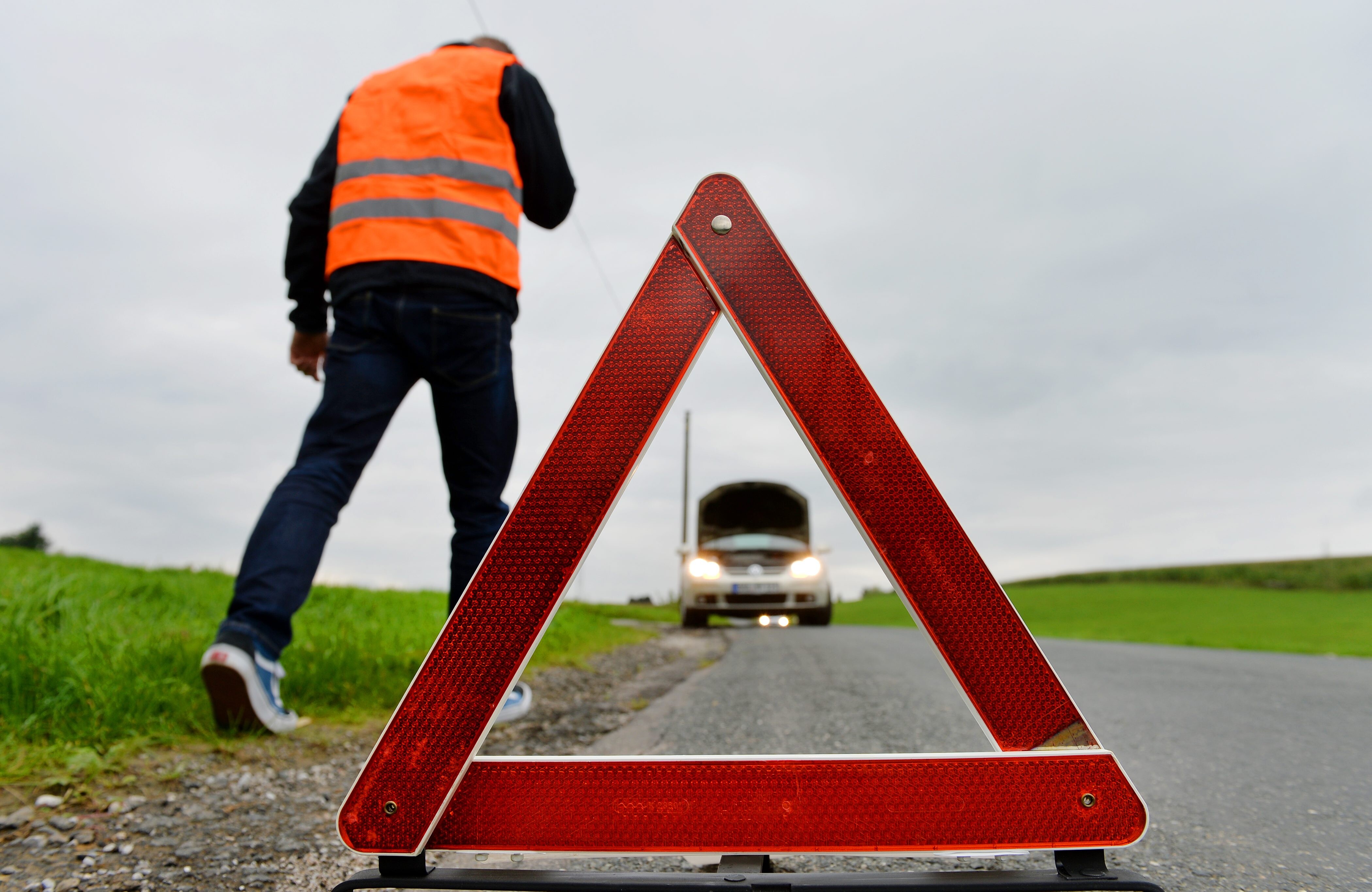 Ein Mann hat eine Autopanne und geht vom aufgestellten Warndreieck zurück zum silbergrauen Wagen.