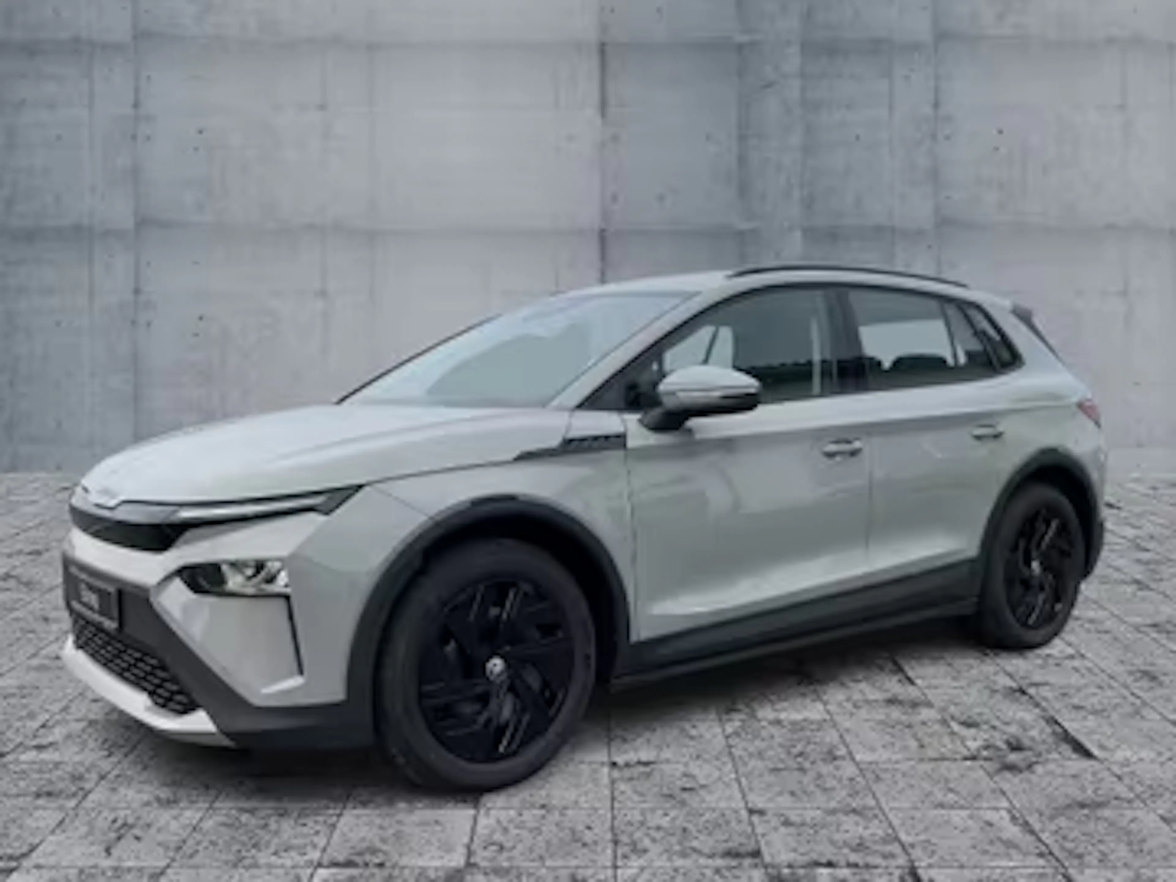 Silberner Skoda Elroq steht vor einer grauen Wand.