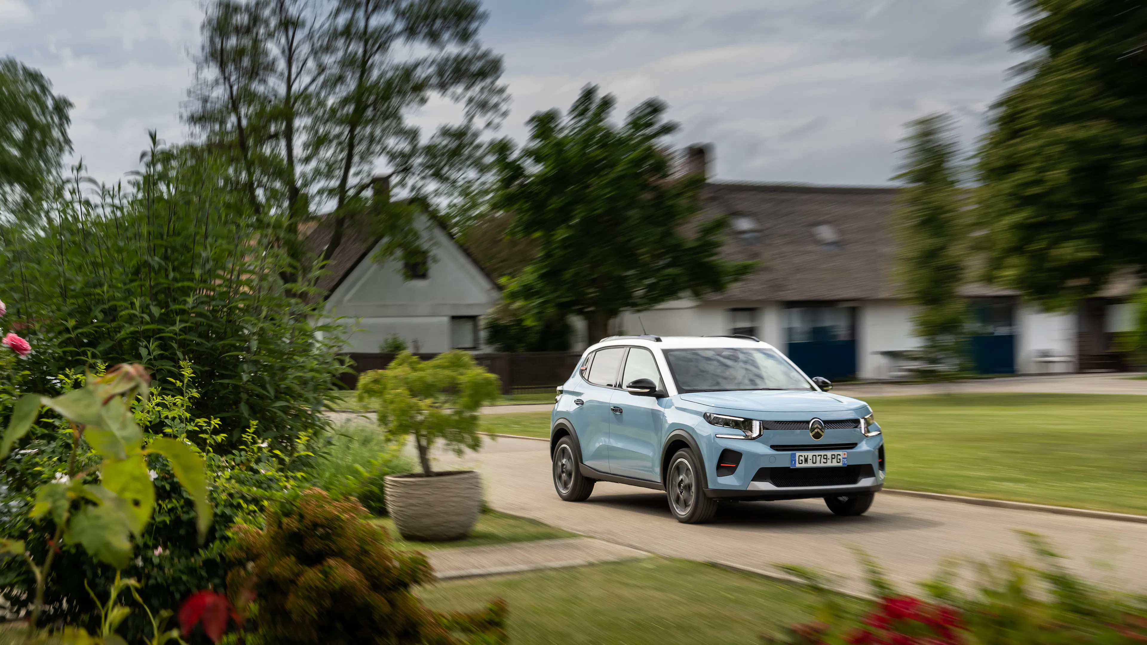 Ein hellblauer Citroën C3 steht auf einer Schotterstraße vor einem kleinen Wohnhaus.