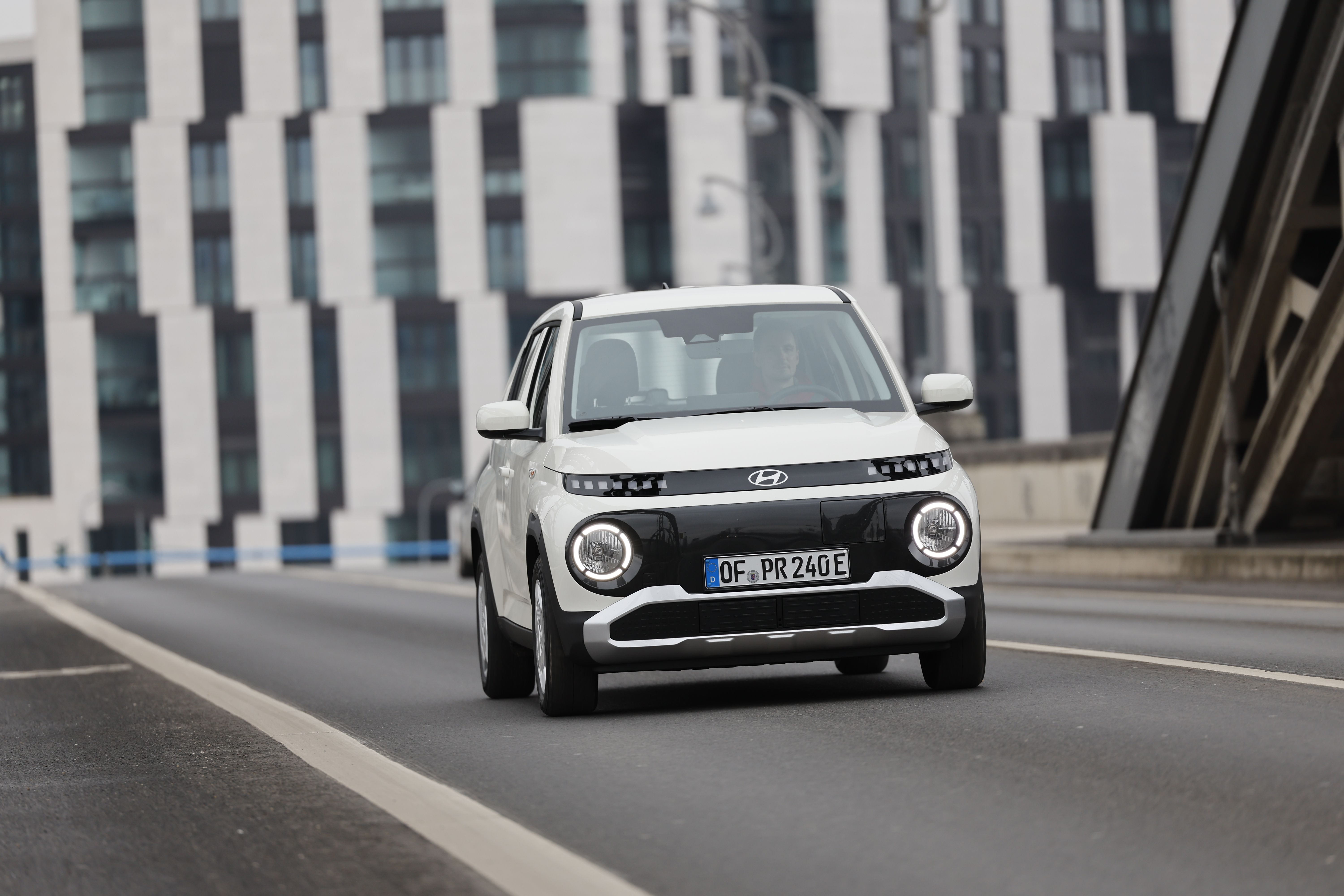 Ein weißer Hyundai Inster fährt auf einer Straße durch die Stadt.
