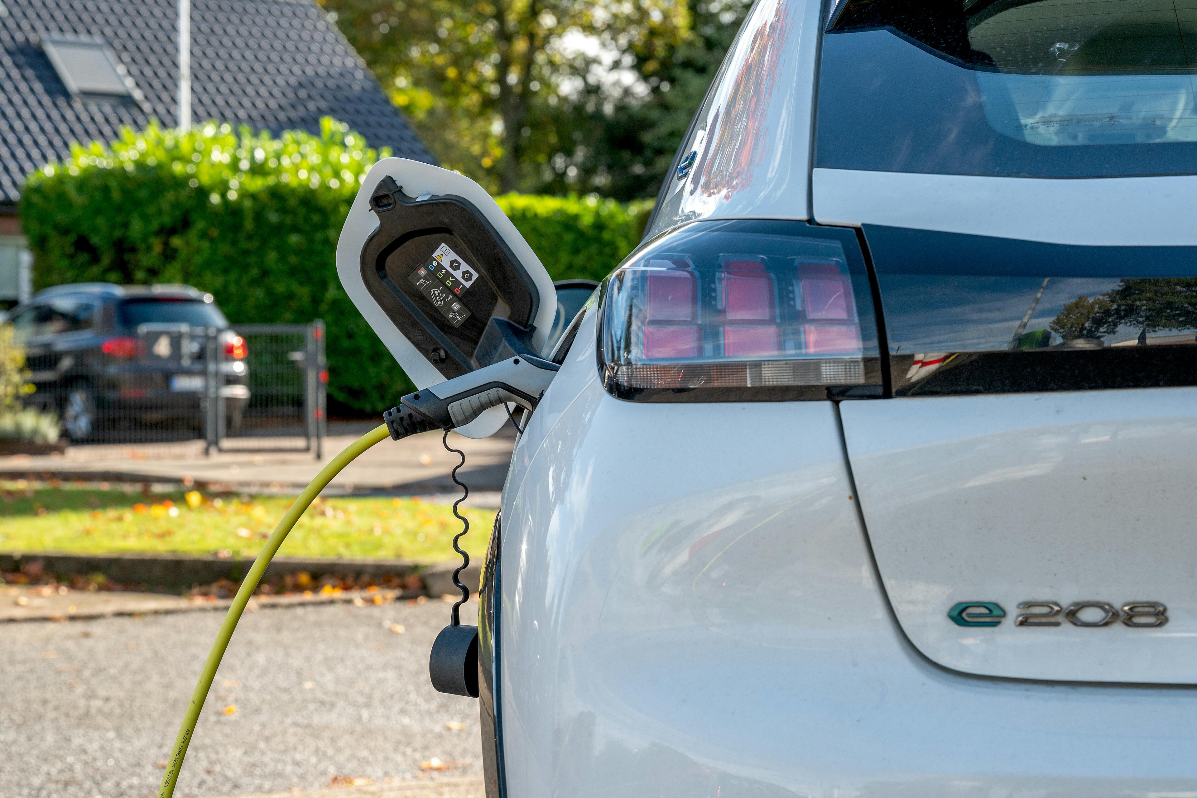 Ein grauer Ladestecker mit gelbem Ladekabel stekt in einem weißen, elektrischen Peugeot e 208.