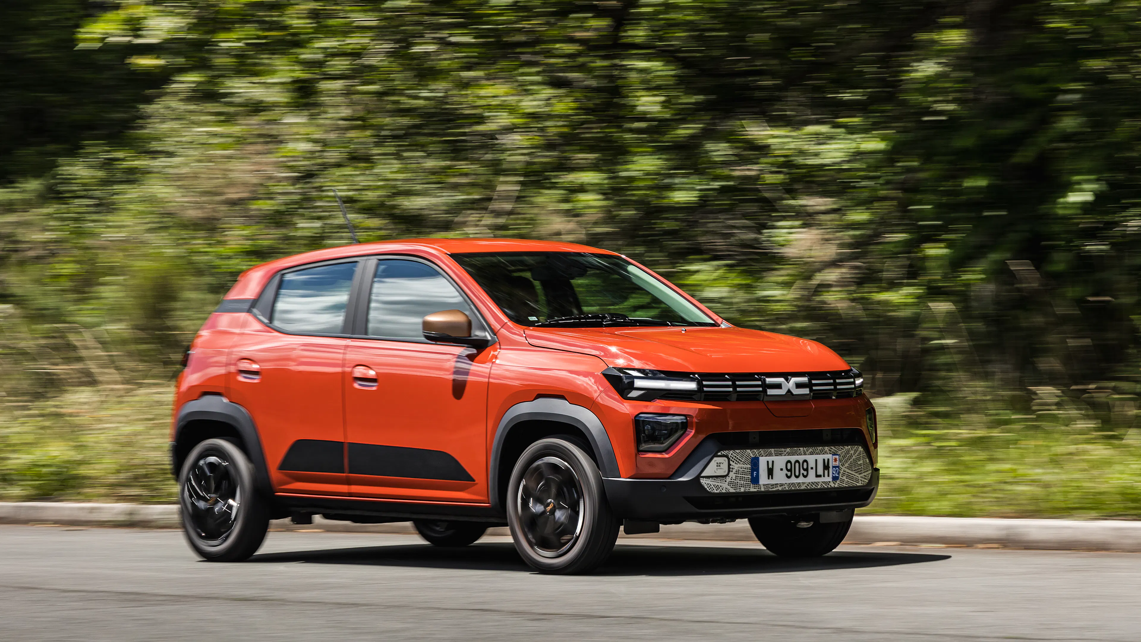 Ein roter Dacia Spring auf einer Straße vor Bäumen