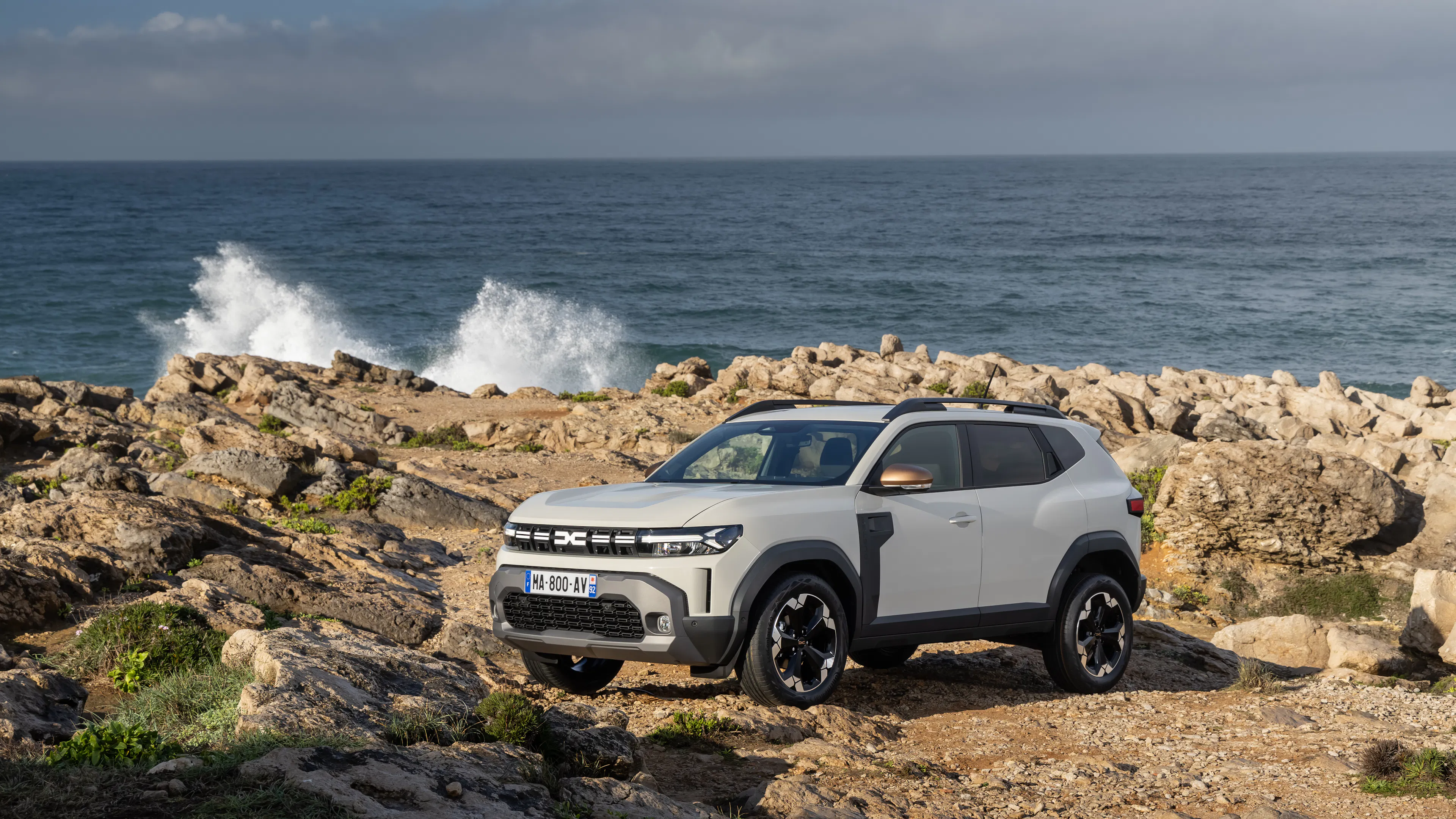 Ein hell lackierter Dacia Duster steht an der Küste