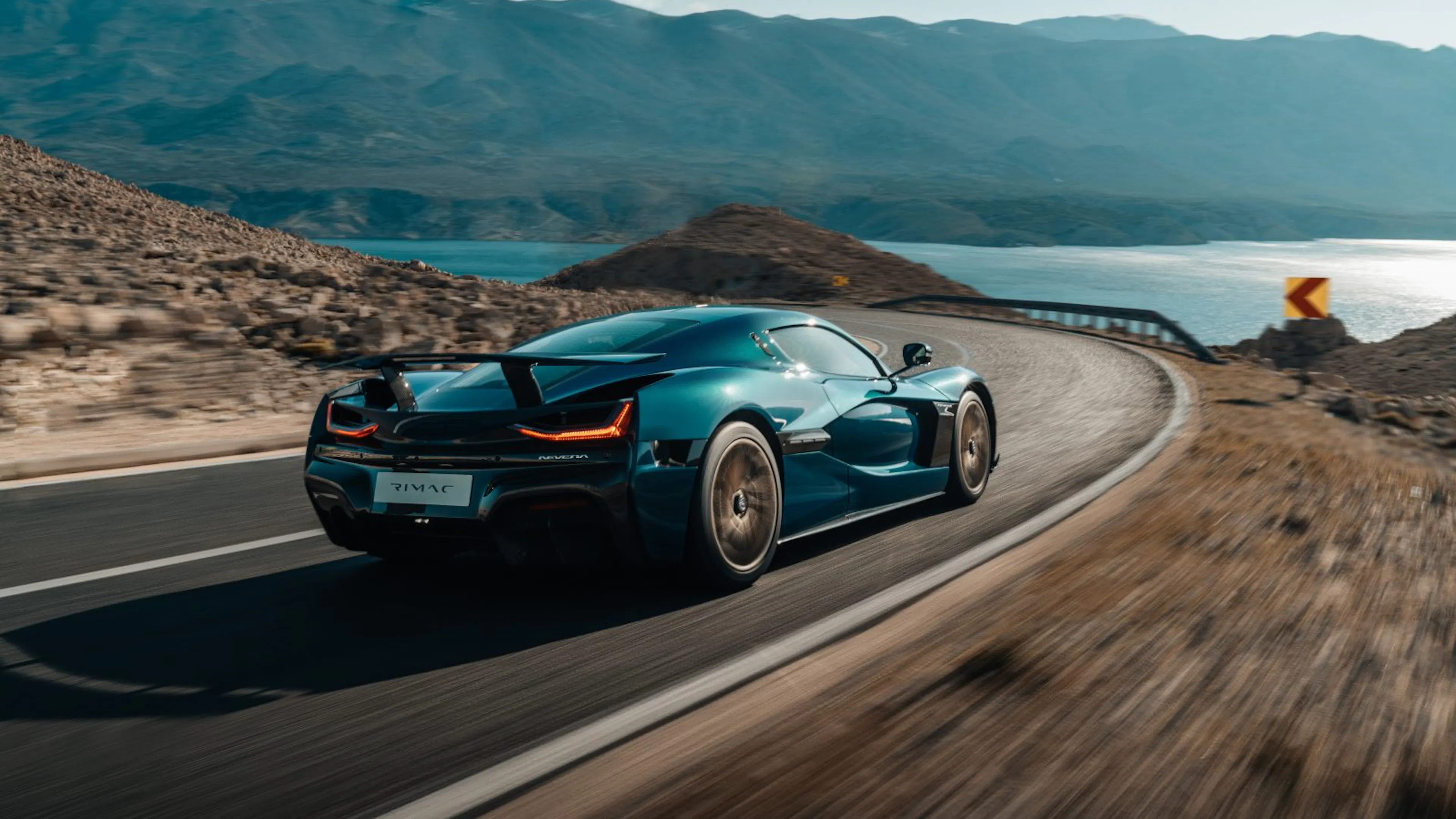 Ein petrolfarbener Rimac Nevera fährt eine Küstenstraße entlang