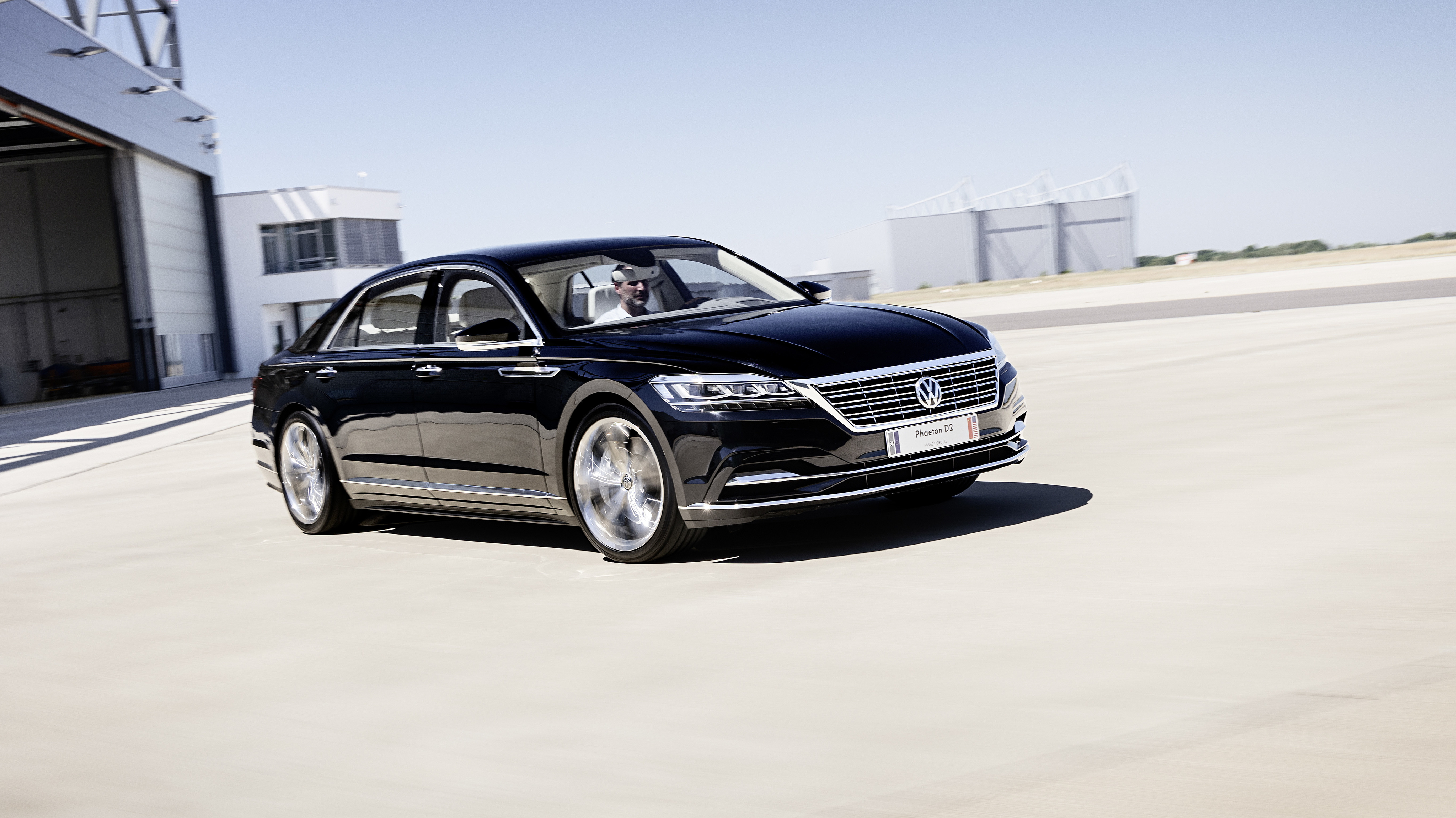 Ein schwarzer VW Phaeton fährt auf einer freien Asphaltfläche.