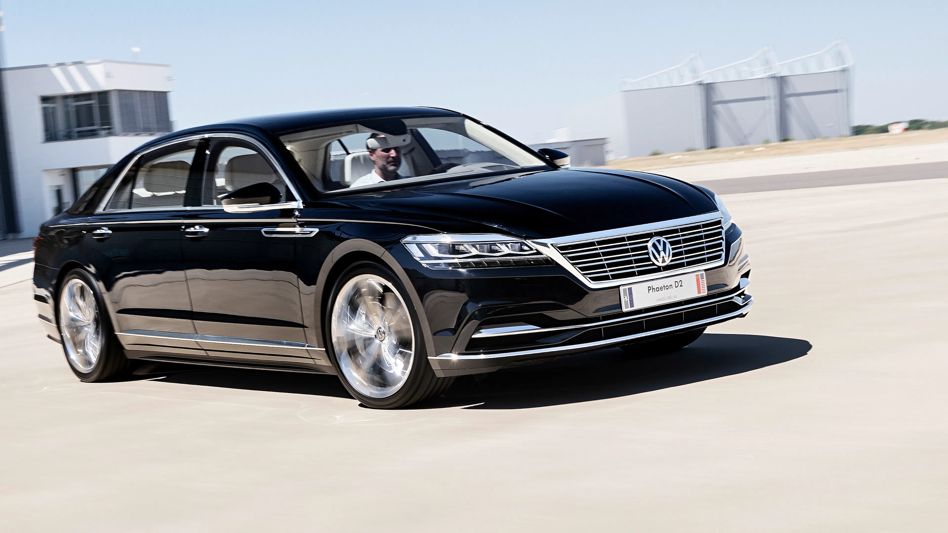 Ein schwarzer VW Phaeton fährt auf einer freien Asphaltfläche.